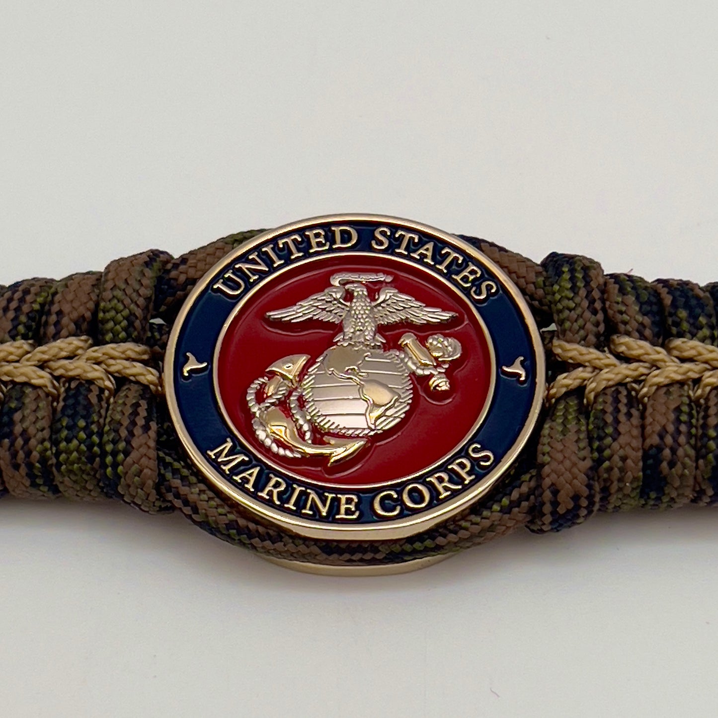 Thick, semi-rigid and comfortable braided United States Marine Corps bracelet featuring a 24K gold and silver plated USMC officer Eagle Globe and Anchor medallion, a gold Cobra style tactical buckle and woven with Woodland Camo 550 paracord and gold micro cord.