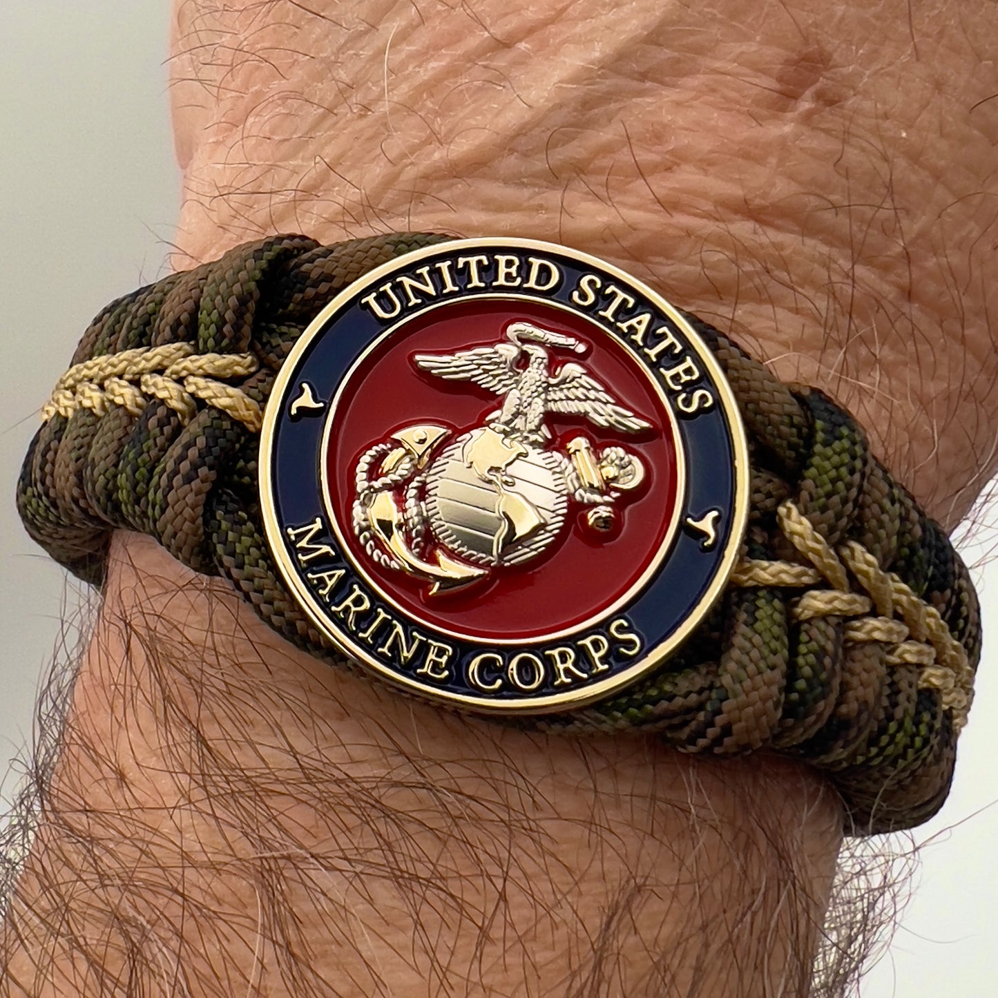 Thick, semi-rigid and comfortable braided United States Marine Corps bracelet featuring a 24K gold and silver plated USMC officer Eagle Globe and Anchor medallion, a gold Cobra style tactical buckle and woven with Woodland Camo 550 paracord and gold micro cord.