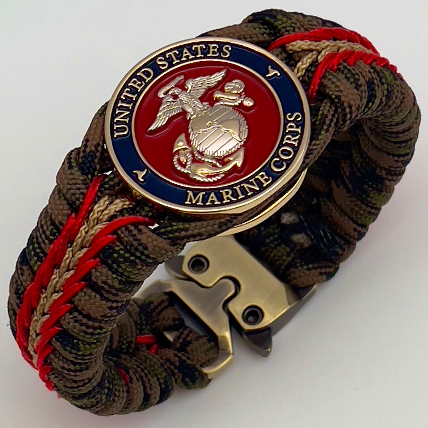 Thick, semi-rigid and comfortable braided United States Marine Corps bracelet featuring a 24K gold and silver plated USMC officer Eagle Globe and Anchor medallion, a gold Cobra style tactical buckle and woven with Woodland Camo 550 paracord and Imperial Red and gold micro cord.