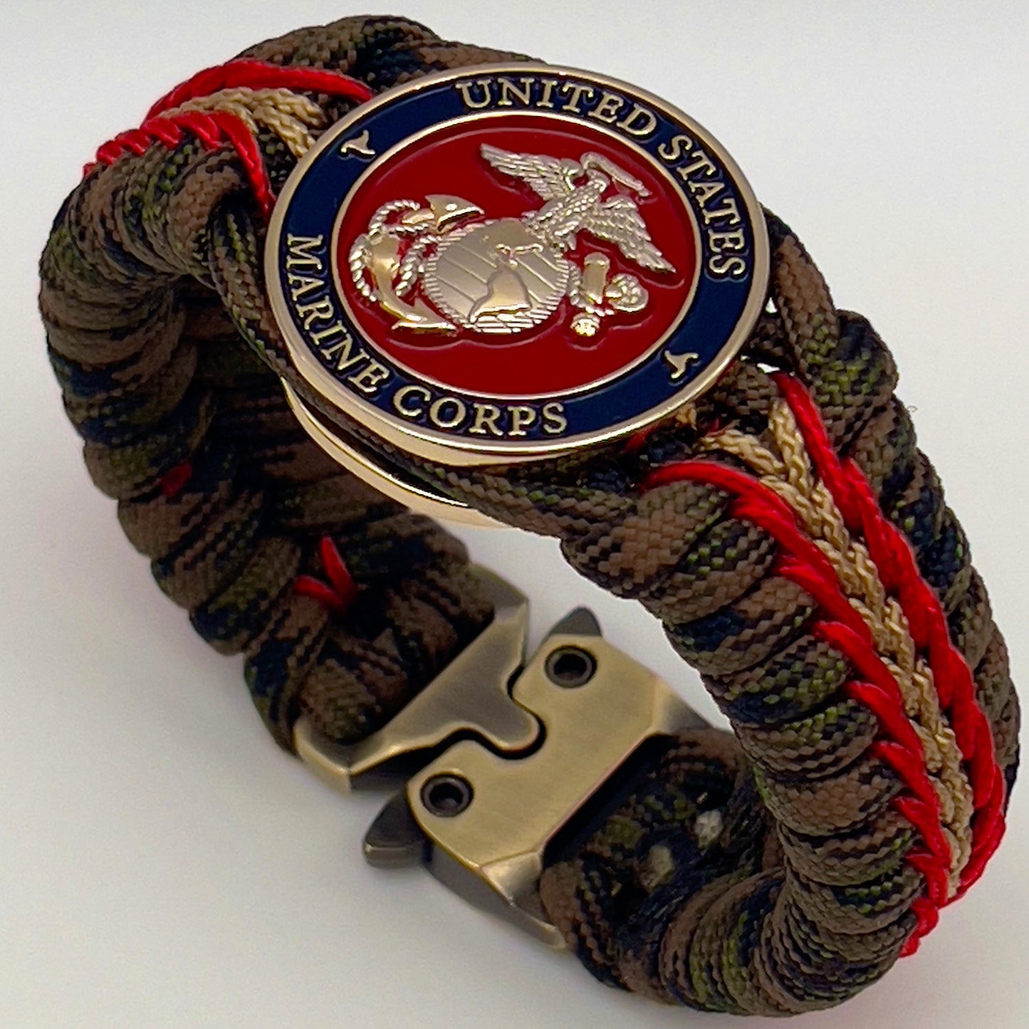 Thick, semi-rigid and comfortable braided United States Marine Corps bracelet featuring a 24K gold and silver plated USMC officer Eagle Globe and Anchor medallion, a gold Cobra style tactical buckle and woven with Woodland Camo 550 paracord and Imperial Red and gold micro cord.
