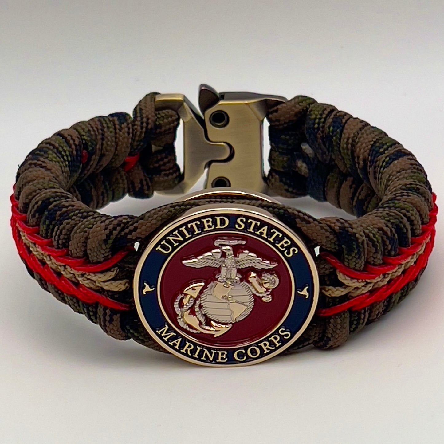 Thick, semi-rigid and comfortable braided United States Marine Corps bracelet featuring a 24K gold and silver plated USMC officer Eagle Globe and Anchor medallion, a gold Cobra style tactical buckle and woven with Woodland Camo 550 paracord and Imperial Red and gold micro cord.