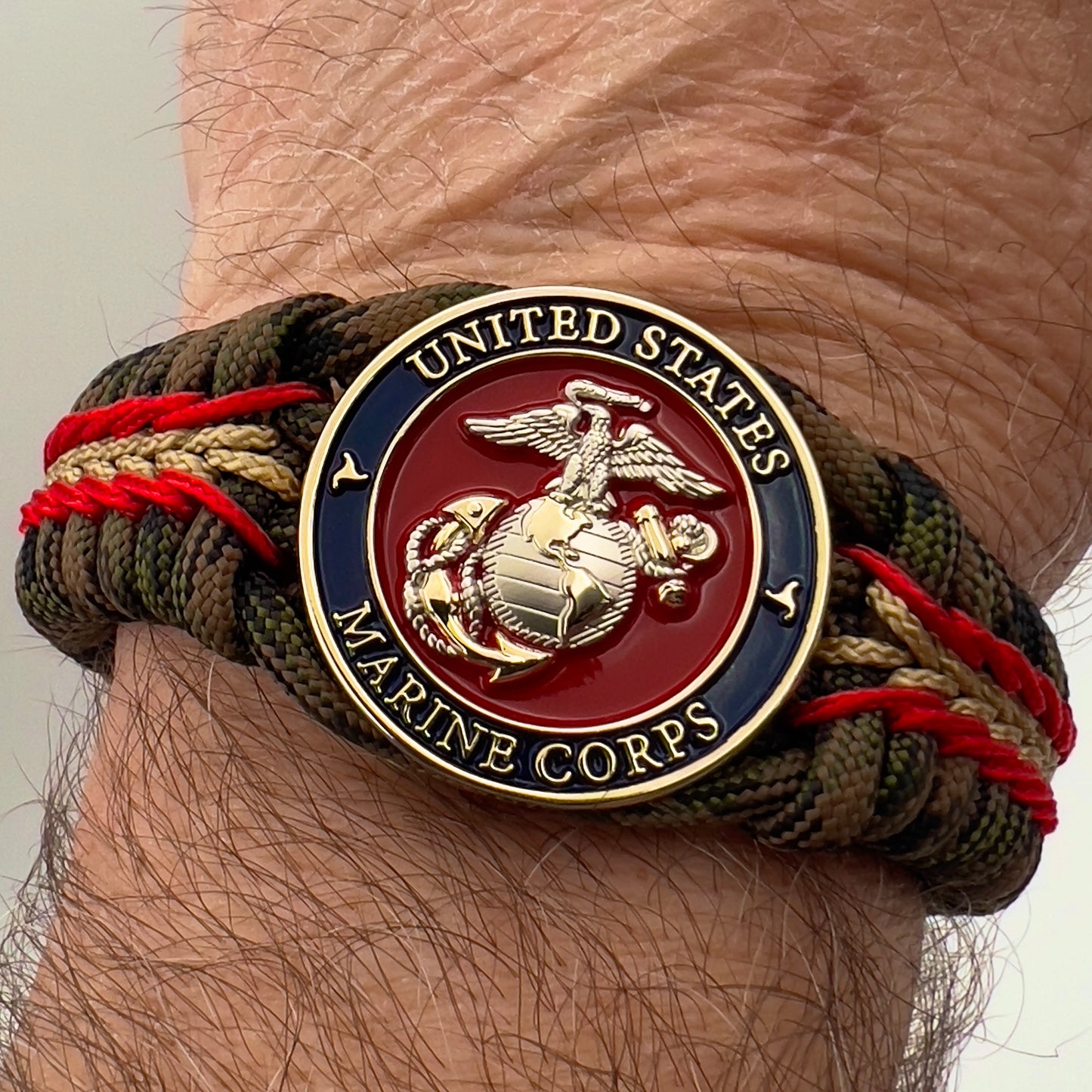 Thick, semi-rigid and comfortable braided United States Marine Corps bracelet featuring a 24K gold and silver plated USMC officer Eagle Globe and Anchor medallion, a gold Cobra style tactical buckle and woven with Woodland Camo 550 paracord and Imperial Red and gold micro cord.