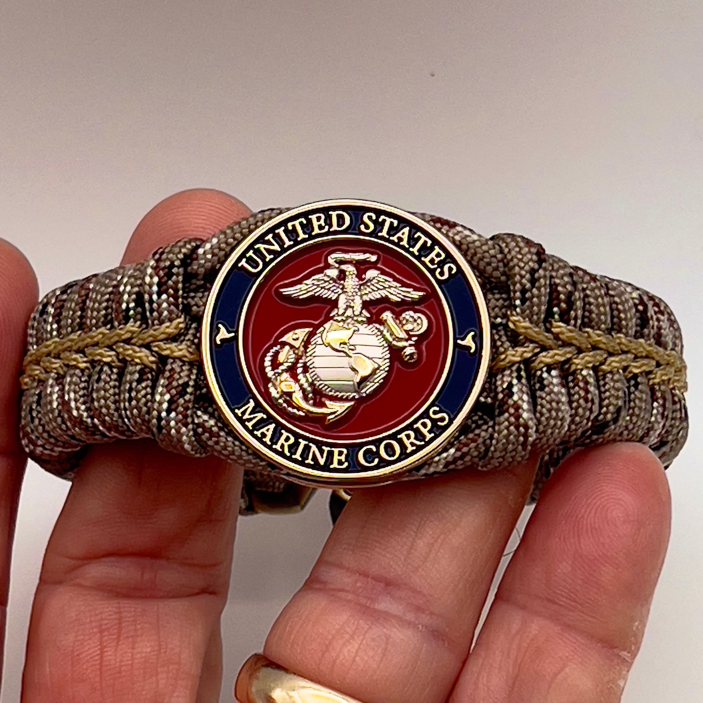 Thick and comfortable braided United States Marine Corps bracelet featuring a 24K gold and silver plated USMC officer Eagle Globe and Anchor medallion, a Cobra style tactical buckle and woven with Desert Camo 550 paracord gold micro cord.