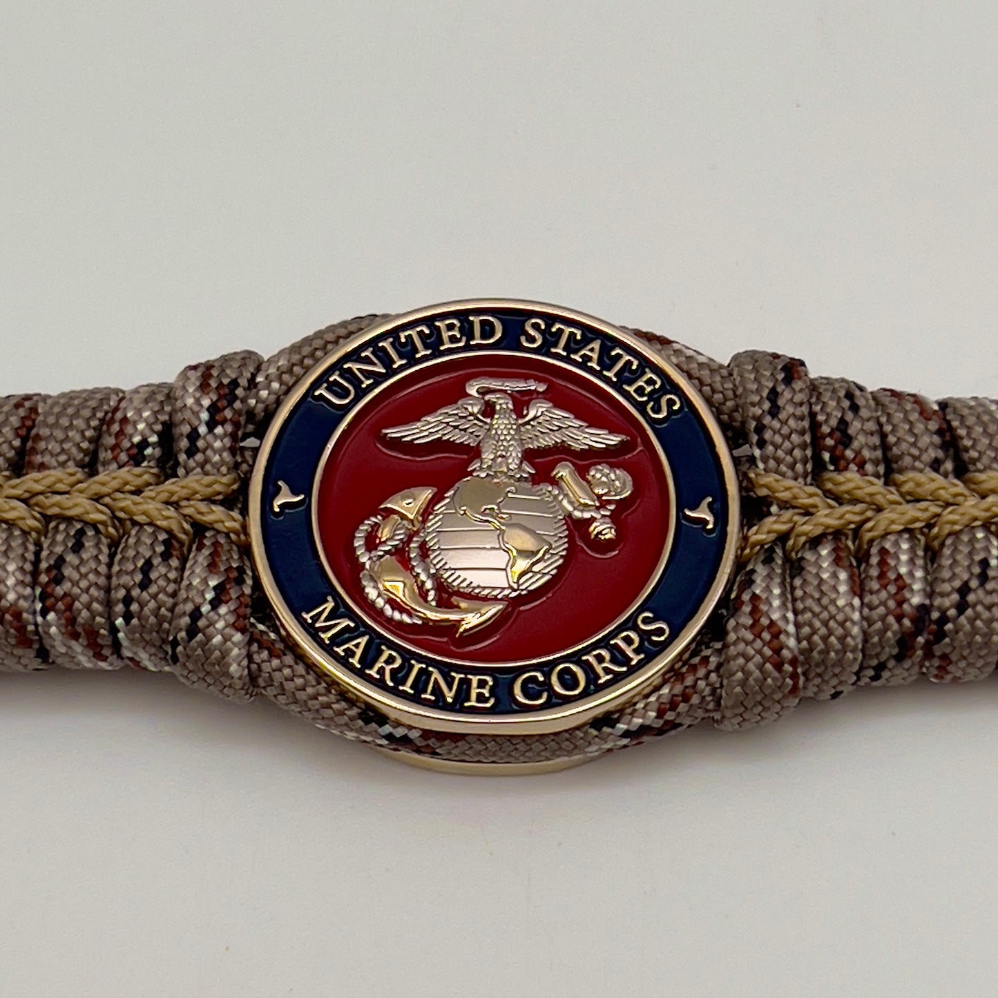 Thick and comfortable braided United States Marine Corps bracelet featuring a 24K gold and silver plated USMC officer Eagle Globe and Anchor medallion, a Cobra style tactical buckle and woven with Desert Camo 550 paracord gold micro cord.