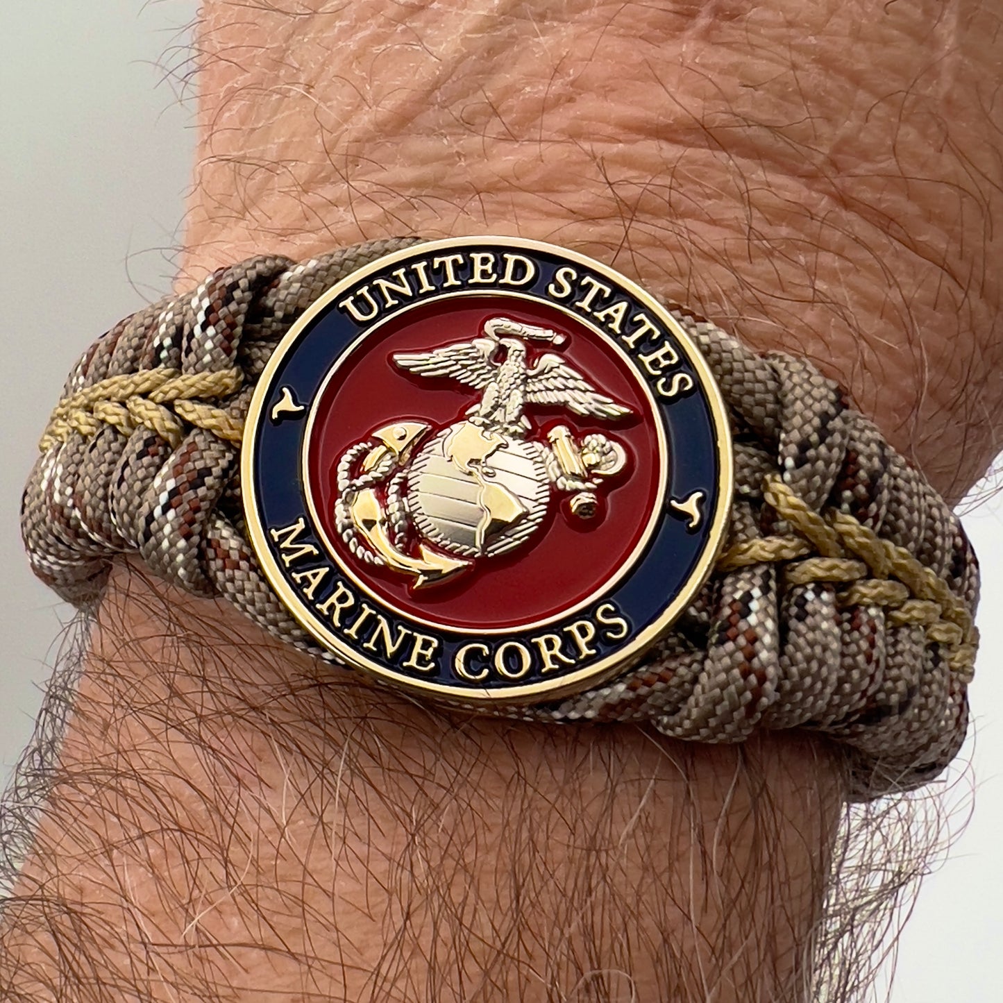 Thick and comfortable braided United States Marine Corps bracelet featuring a 24K gold and silver plated USMC officer Eagle Globe and Anchor medallion, a Cobra style tactical buckle and woven with Desert Camo 550 paracord gold micro cord.