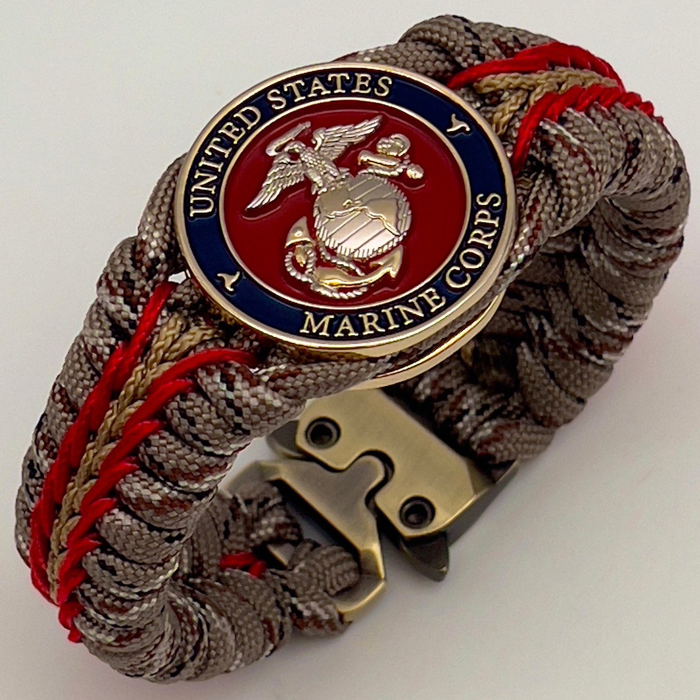 Thick and comfortable braided United States Marine Corps bracelet featuring a 24K gold and silver plated USMC officer Eagle Globe and Anchor medallion, a Cobra style tactical buckle and woven with Desert Camo 550 paracord and Imperial red and gold micro cord.