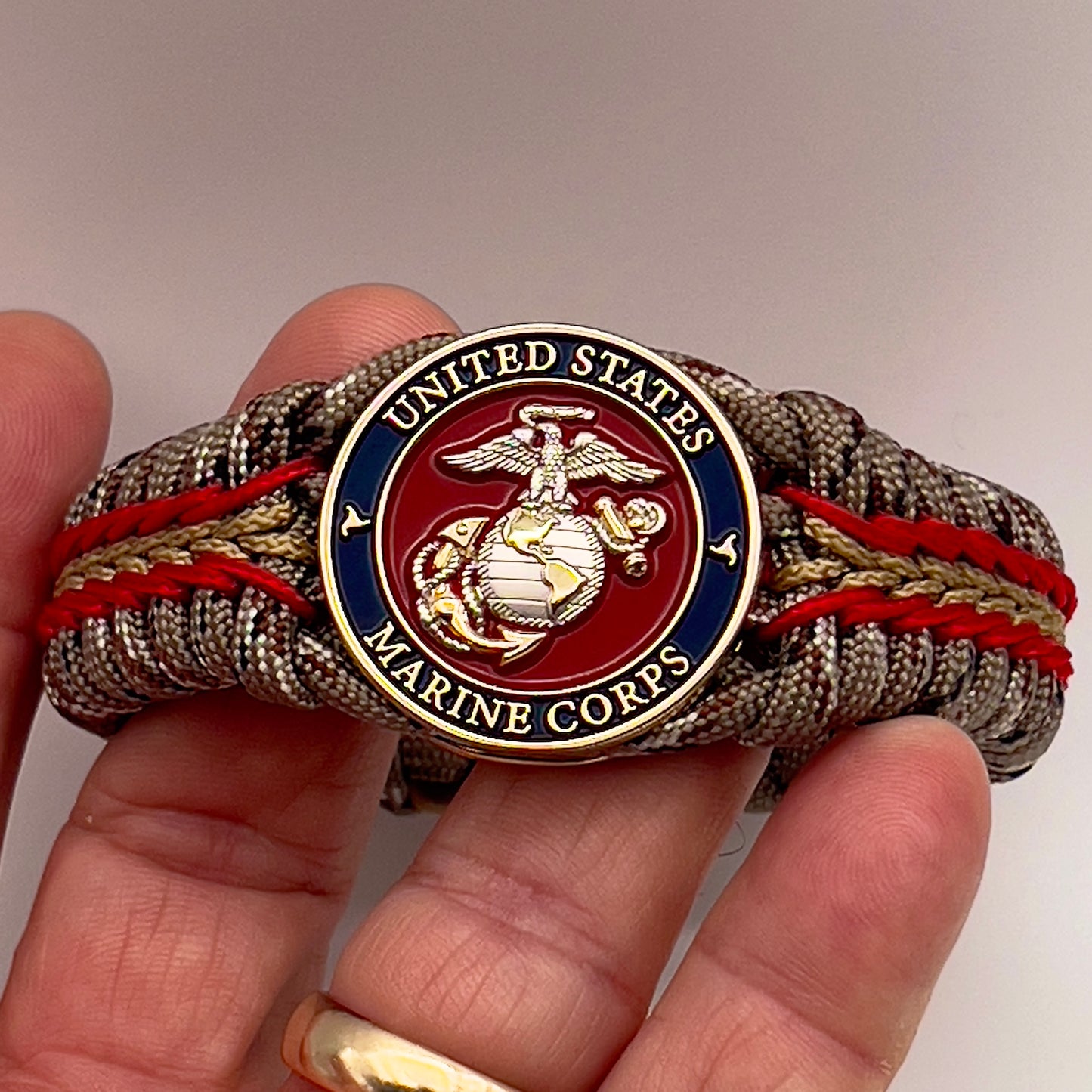 Thick and comfortable braided United States Marine Corps bracelet featuring a 24K gold and silver plated USMC officer Eagle Globe and Anchor medallion, a Cobra style tactical buckle and woven with Desert Camo 550 paracord and Imperial red and gold micro cord.