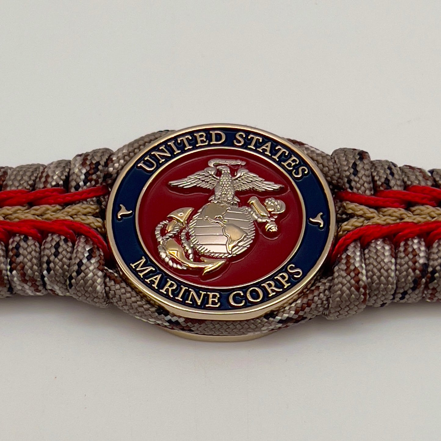 Thick and comfortable braided United States Marine Corps bracelet featuring a 24K gold and silver plated USMC officer Eagle Globe and Anchor medallion, a Cobra style tactical buckle and woven with Desert Camo 550 paracord and Imperial red and gold micro cord.