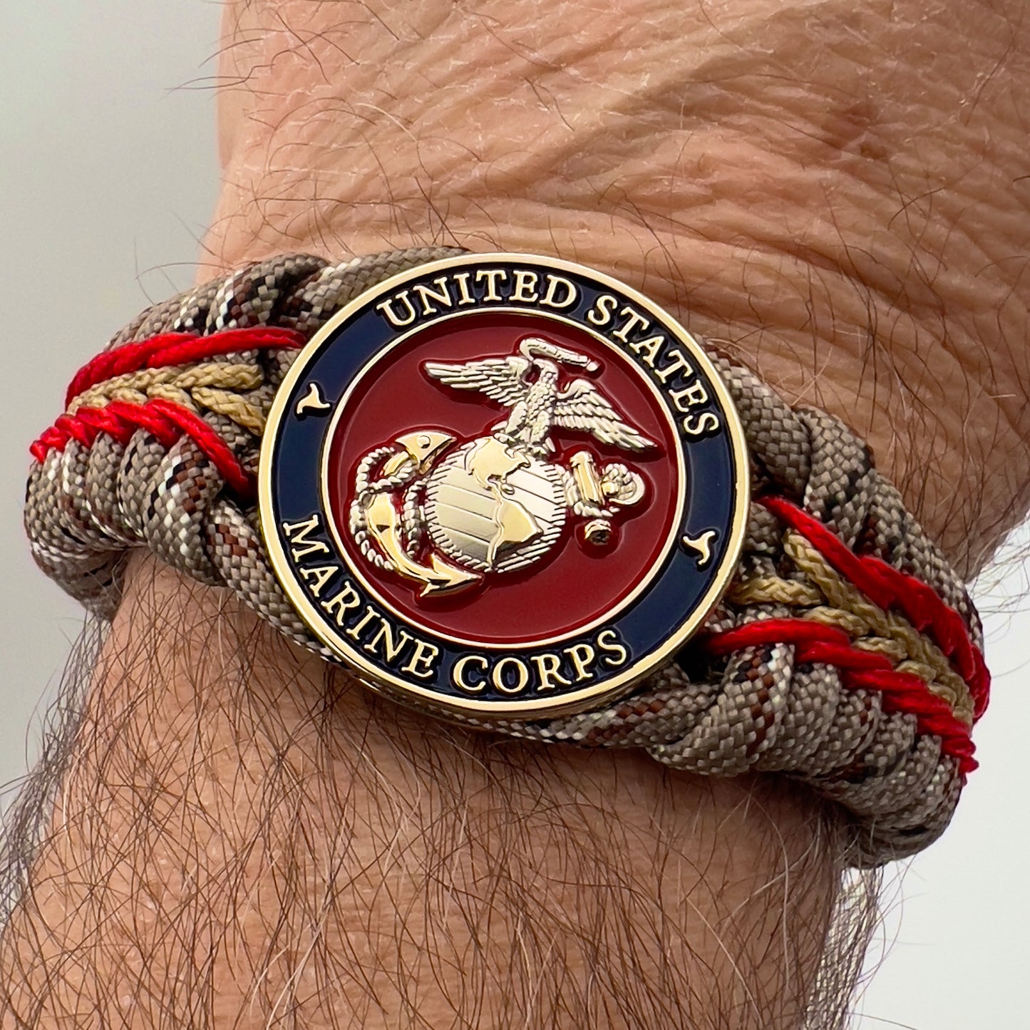 Thick and comfortable braided United States Marine Corps bracelet featuring a 24K gold and silver plated USMC officer Eagle Globe and Anchor medallion, a Cobra style tactical buckle and woven with Desert Camo 550 paracord and Imperial red and gold micro cord.