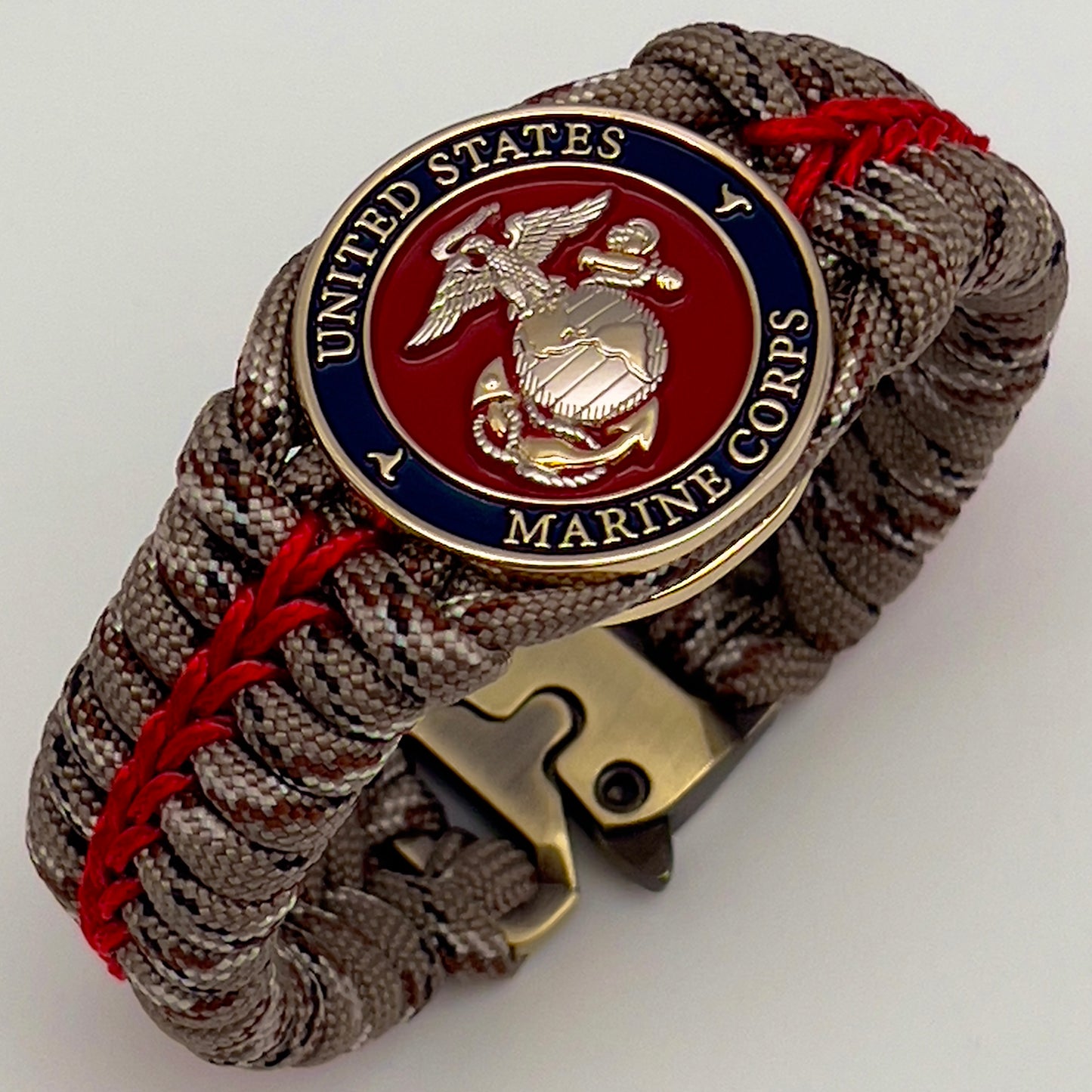 Thick and comfortable braided United States Marine Corps bracelet featuring a 24K gold and silver plated USMC officer Eagle Globe and Anchor medallion, a Cobra style tactical buckle and woven with Desert Camo 550 paracord and Imperial red micro cord.