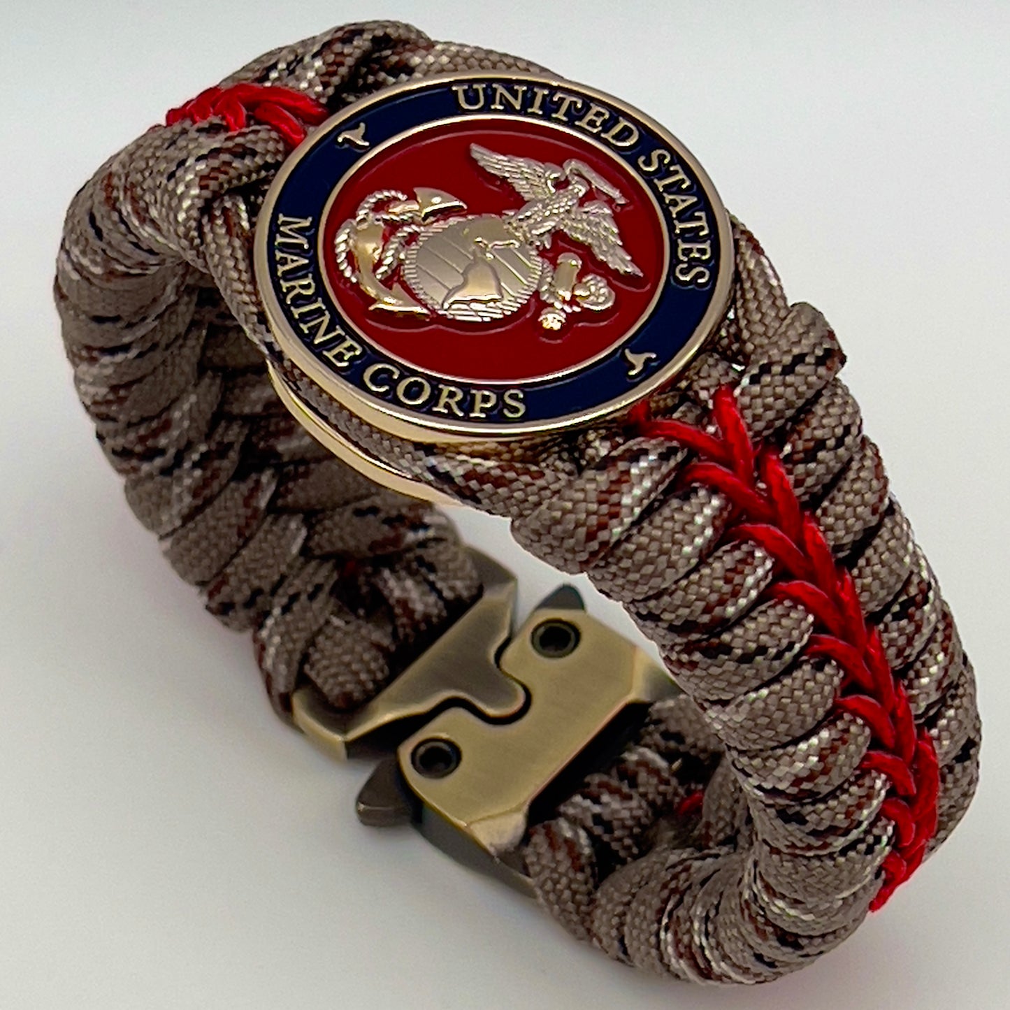 Thick and comfortable braided United States Marine Corps bracelet featuring a 24K gold and silver plated USMC officer Eagle Globe and Anchor medallion, a Cobra style tactical buckle and woven with Desert Camo 550 paracord and Imperial red micro cord.