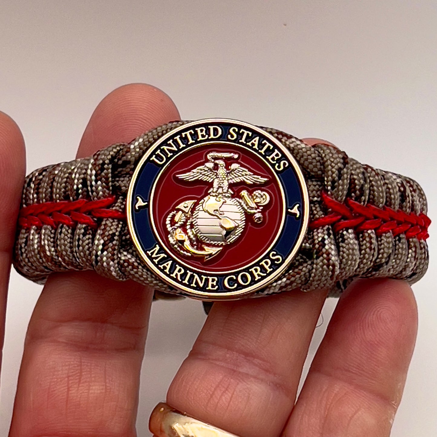 Thick and comfortable braided United States Marine Corps bracelet featuring a 24K gold and silver plated USMC officer Eagle Globe and Anchor medallion, a Cobra style tactical buckle and woven with Desert Camo 550 paracord and Imperial red micro cord.
