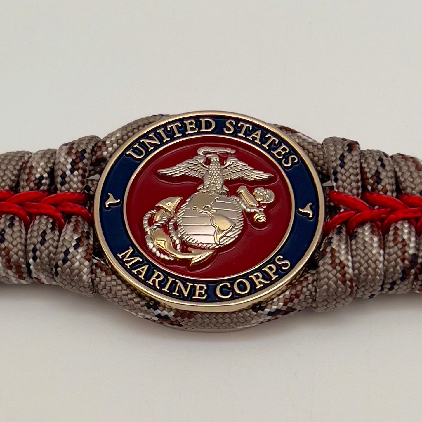 Thick and comfortable braided United States Marine Corps bracelet featuring a 24K gold and silver plated USMC officer Eagle Globe and Anchor medallion, a Cobra style tactical buckle and woven with Desert Camo 550 paracord and Imperial red micro cord.