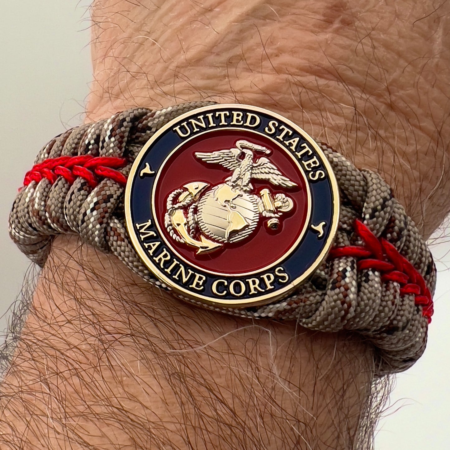 Thick and comfortable braided United States Marine Corps bracelet featuring a 24K gold and silver plated USMC officer Eagle Globe and Anchor medallion, a Cobra style tactical buckle and woven with Desert Camo 550 paracord and Imperial red micro cord.