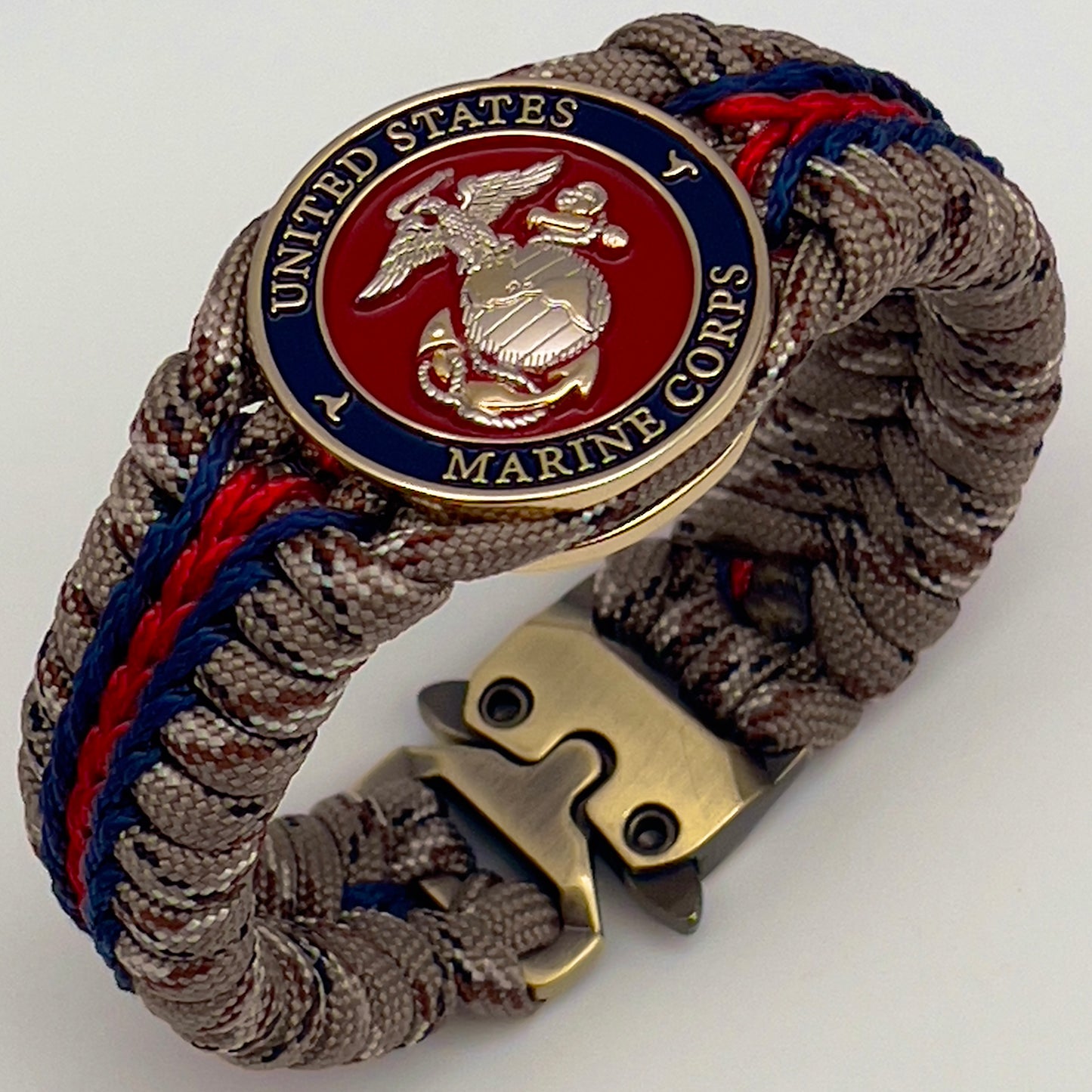 Thick and comfortable braided United States Marine Corps bracelet featuring a 24K gold and silver plated USMC officer Eagle Globe and Anchor medallion, a Cobra style tactical buckle and woven with Desert Camo 550 paracord and Imperial red and Navy Blue micro cord.