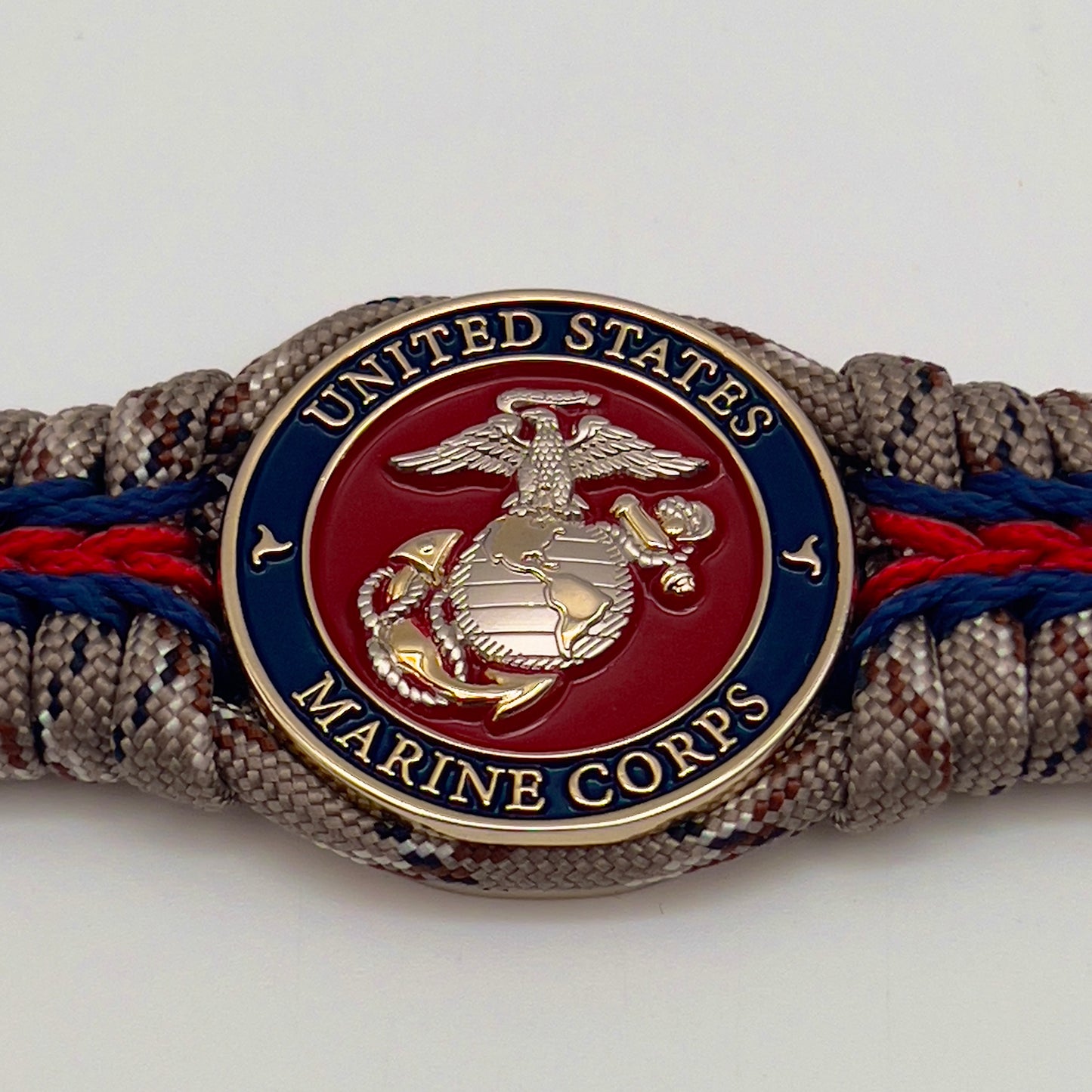Thick and comfortable braided United States Marine Corps bracelet featuring a 24K gold and silver plated USMC officer Eagle Globe and Anchor medallion, a Cobra style tactical buckle and woven with Desert Camo 550 paracord and Imperial red and Navy Blue micro cord.