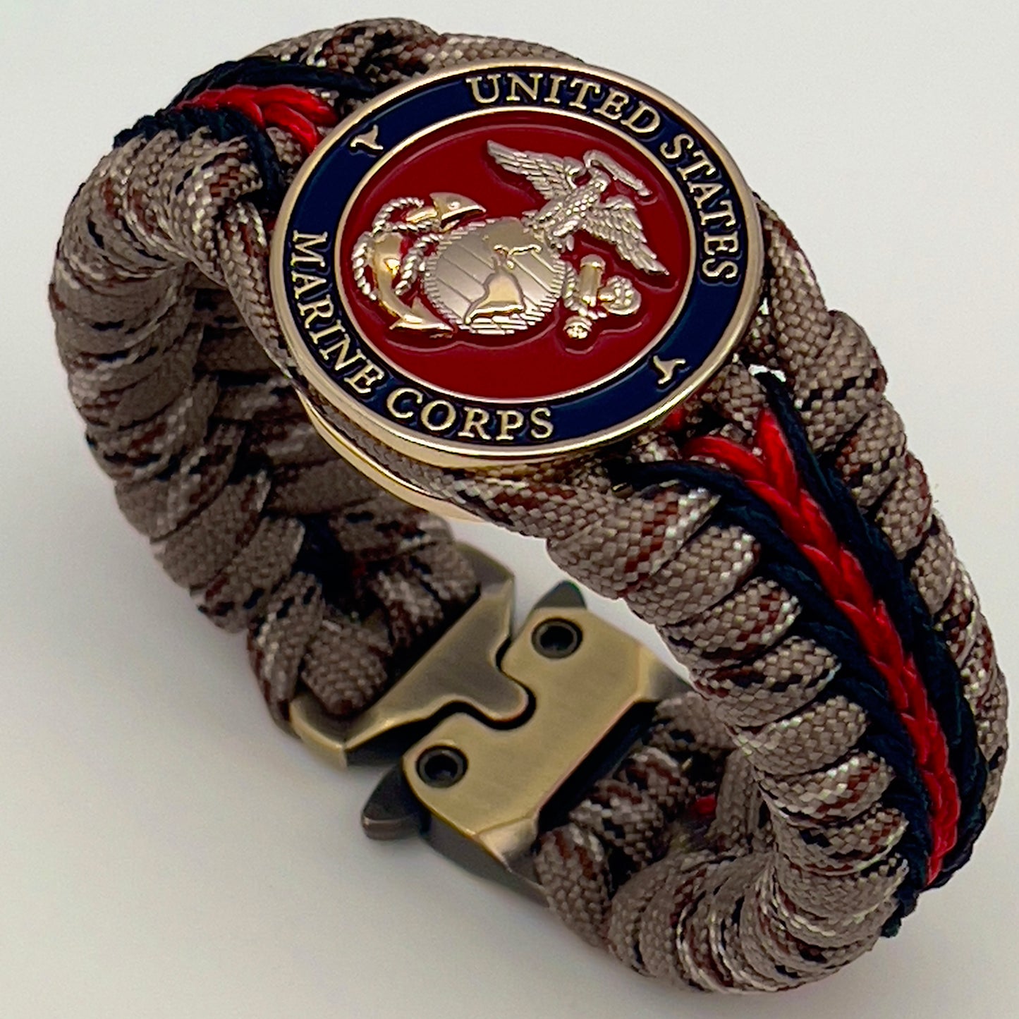 Thick and comfortable braided United States Marine Corps bracelet featuring a 24K gold and silver plated USMC officer Eagle Globe and Anchor medallion, a Cobra style tactical buckle and woven with Desert Camo 550 paracord and Imperial red and black micro cord.