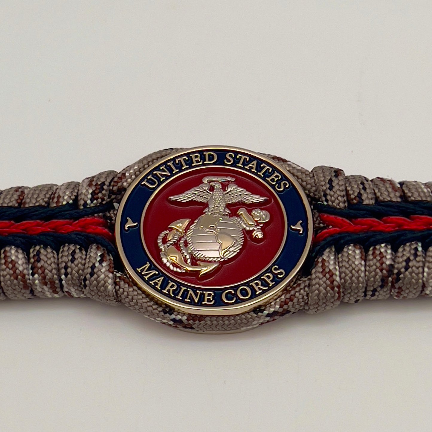 Thick and comfortable braided United States Marine Corps bracelet featuring a 24K gold and silver plated USMC officer Eagle Globe and Anchor medallion, a Cobra style tactical buckle and woven with Desert Camo 550 paracord and Imperial red and black micro cord.