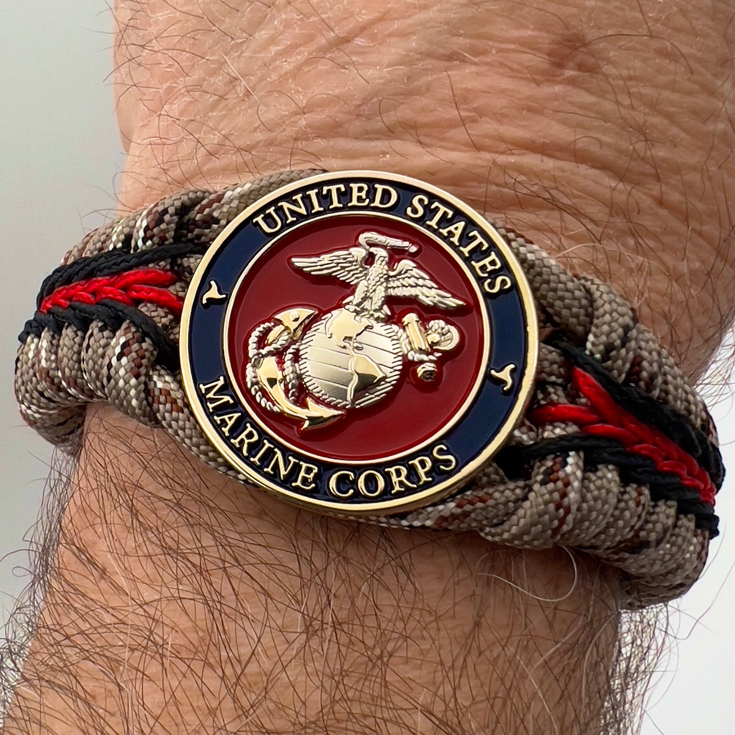 Thick and comfortable braided United States Marine Corps bracelet featuring a 24K gold and silver plated USMC officer Eagle Globe and Anchor medallion, a Cobra style tactical buckle and woven with Desert Camo 550 paracord and Imperial red and black micro cord.