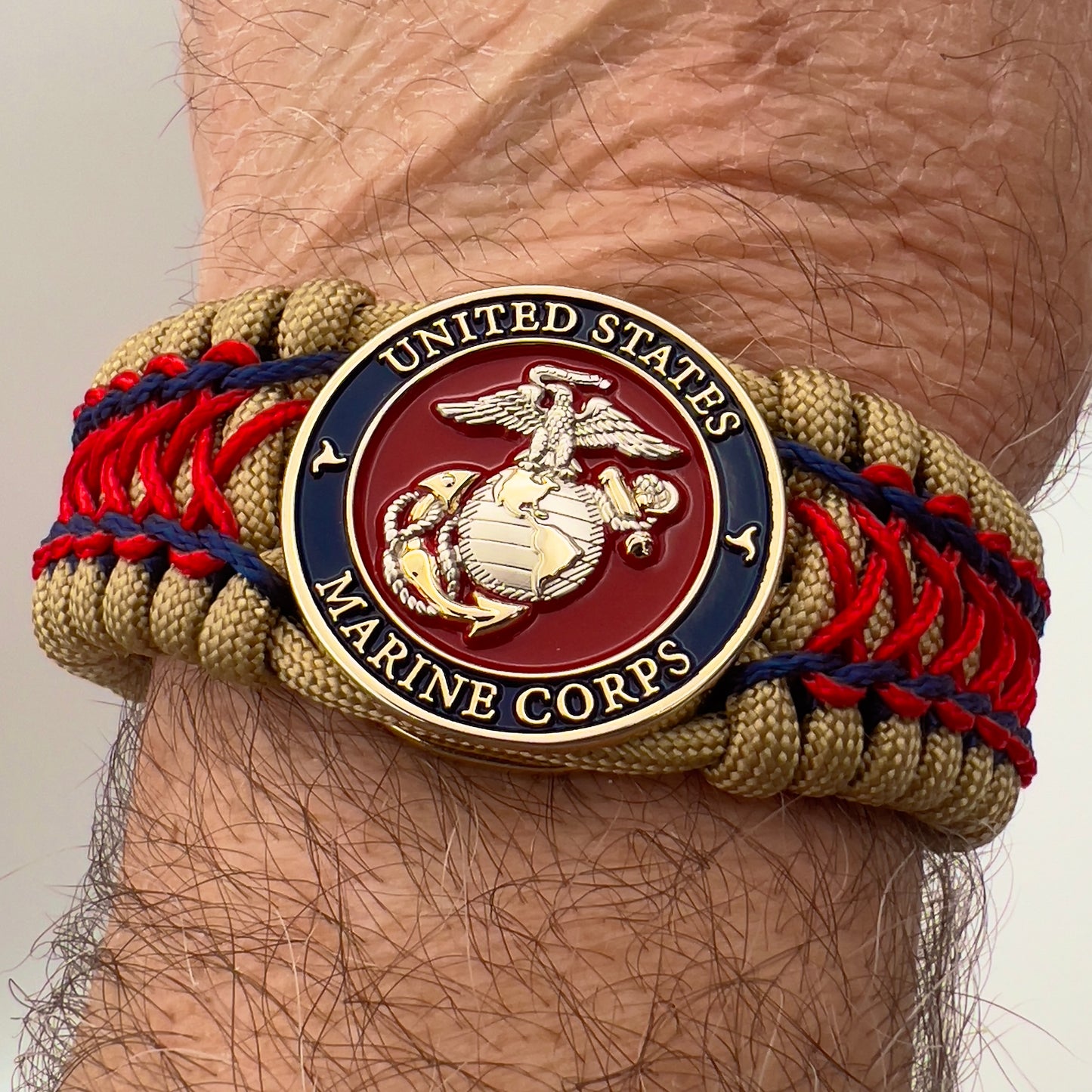 Thick and comfortable braided United States Marine Corps bracelet featuring a 24K gold and silver plated USMC officer Eagle Globe and Anchor medallion, a gold Cobra style tactical buckle and woven with gold 550 paracord and Imperial Red and Navy Blue micro cord.