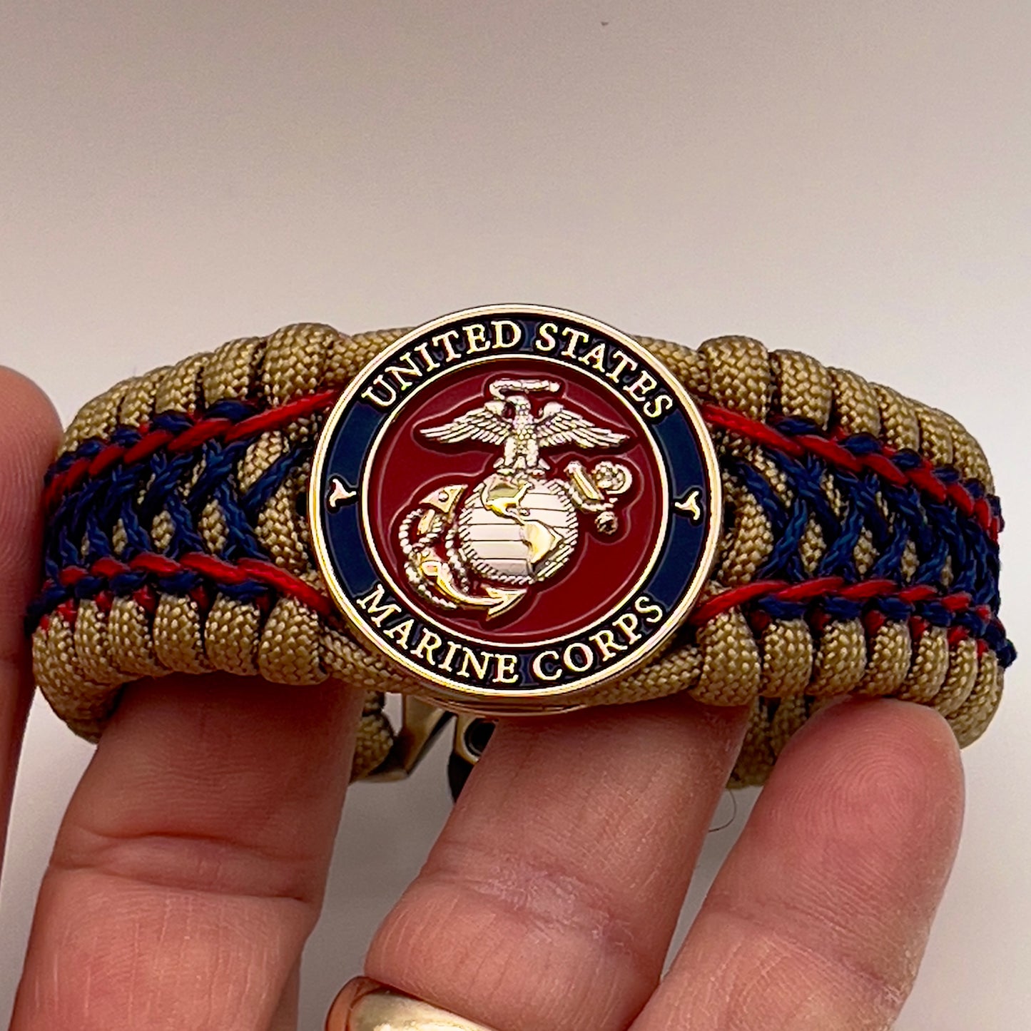 Thick and comfortable braided United States Marine Corps bracelet featuring a 24K gold and silver plated USMC officer Eagle Globe and Anchor medallion, a gold Cobra style tactical buckle and woven with gold 550 paracord and Imperial Red and Navy Blue micro cord.