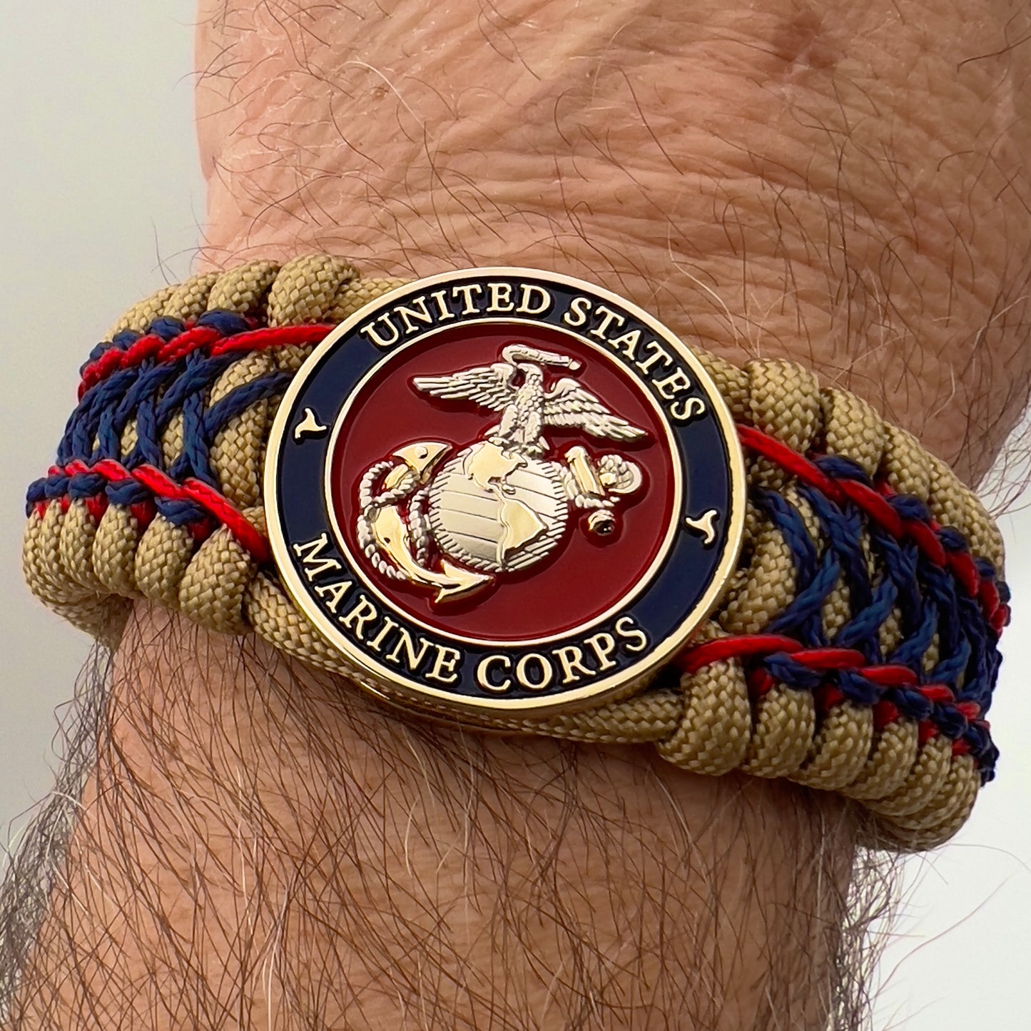 Thick and comfortable braided United States Marine Corps bracelet featuring a 24K gold and silver plated USMC officer Eagle Globe and Anchor medallion, a gold Cobra style tactical buckle and woven with gold 550 paracord and Imperial Red and Navy Blue micro cord.