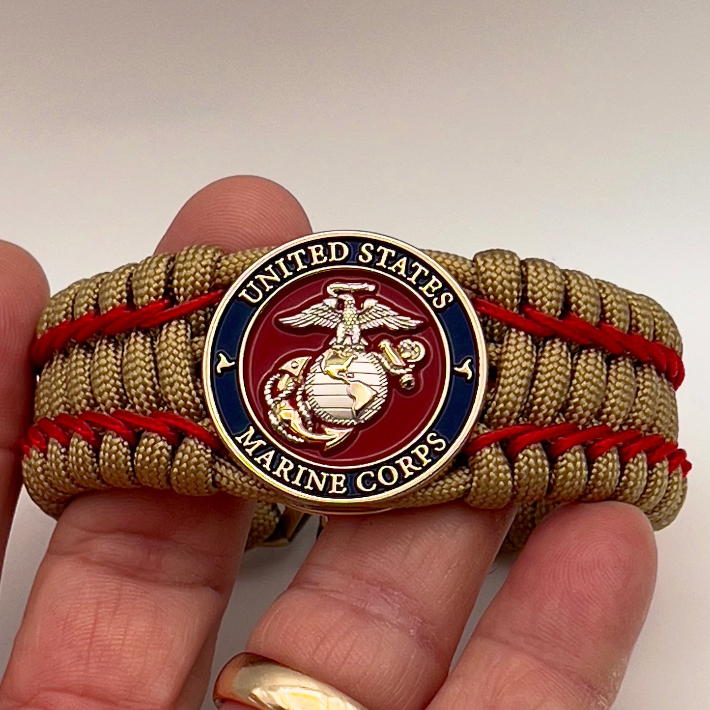 Thick and comfortable braided United States Marine Corps bracelet featuring a 24K gold and silver plated USMC officer Eagle Globe and Anchor medallion, a gold Cobra style tactical buckle and woven with gold 550 paracord and Imperial Red micro cord.