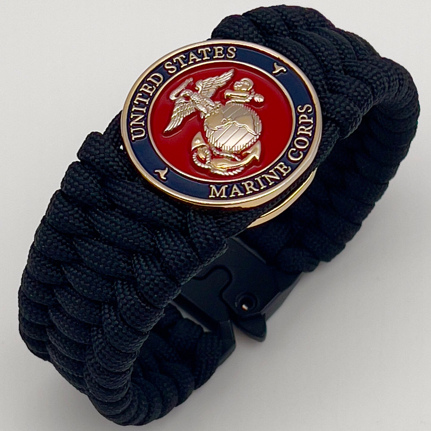Thick and comfortable braided United States Marine Corps bracelet featuring a 24K gold and silver plated USMC officer Eagle Globe and Anchor medallion, a black Cobra style tactical buckle and woven with black 550 paracord.