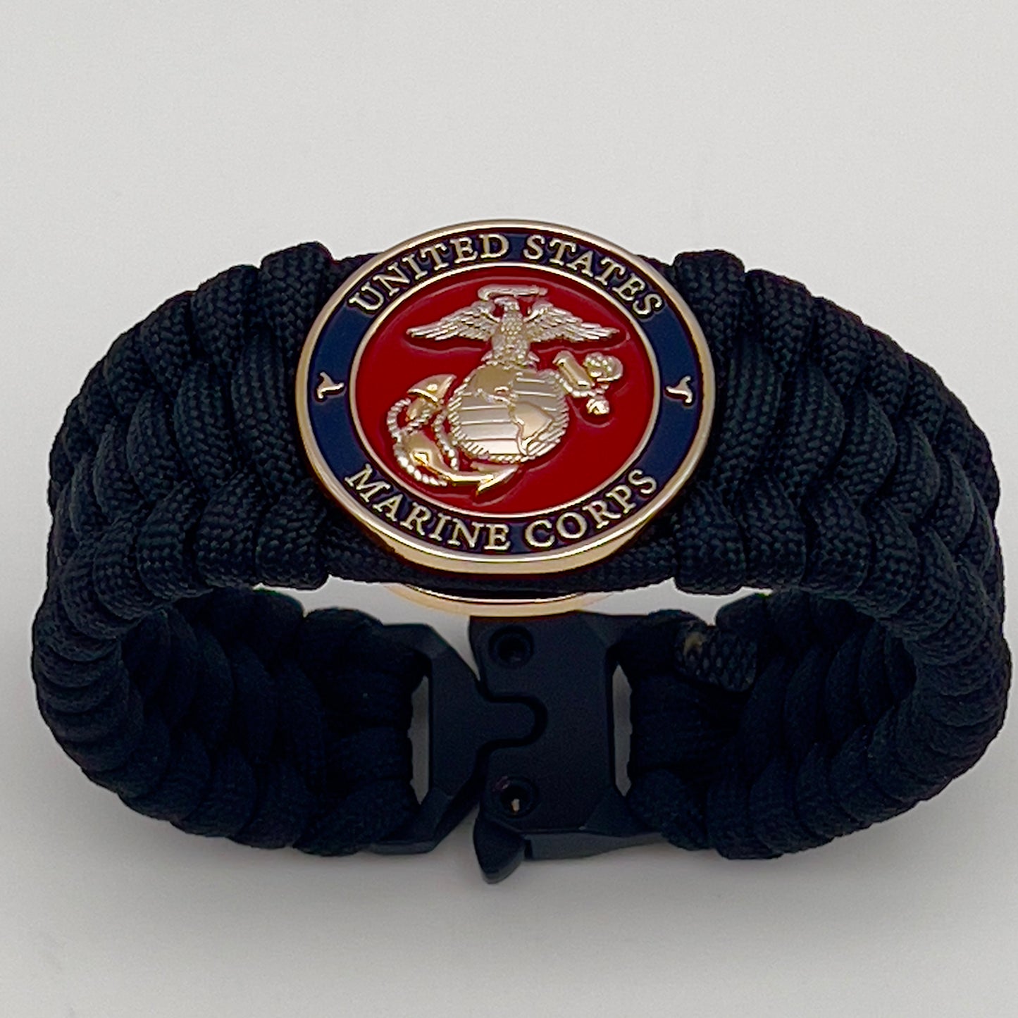 Thick and comfortable braided United States Marine Corps bracelet featuring a 24K gold and silver plated USMC officer Eagle Globe and Anchor medallion, a black Cobra style tactical buckle and woven with black 550 paracord.