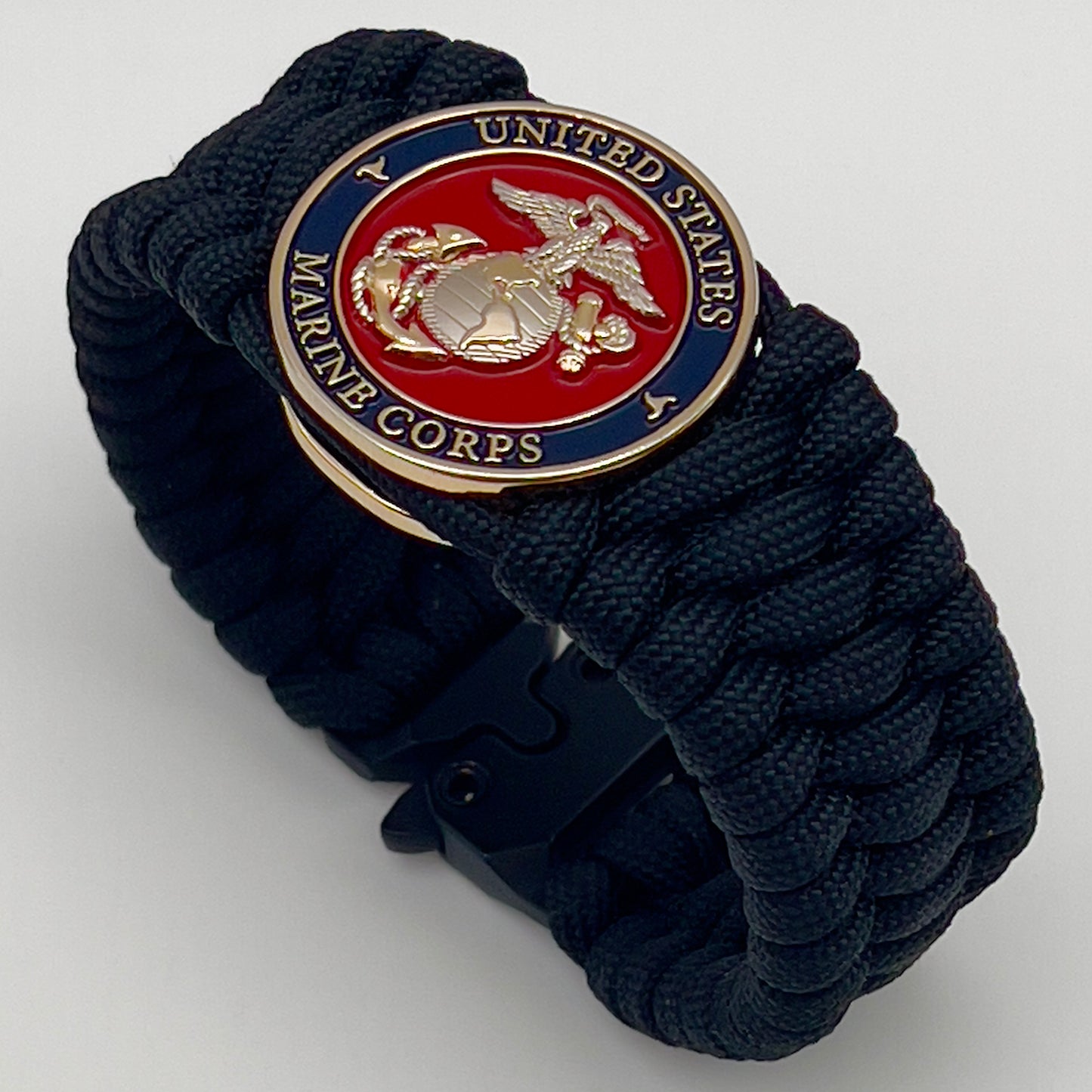 Thick and comfortable braided United States Marine Corps bracelet featuring a 24K gold and silver plated USMC officer Eagle Globe and Anchor medallion, a black Cobra style tactical buckle and woven with black 550 paracord.