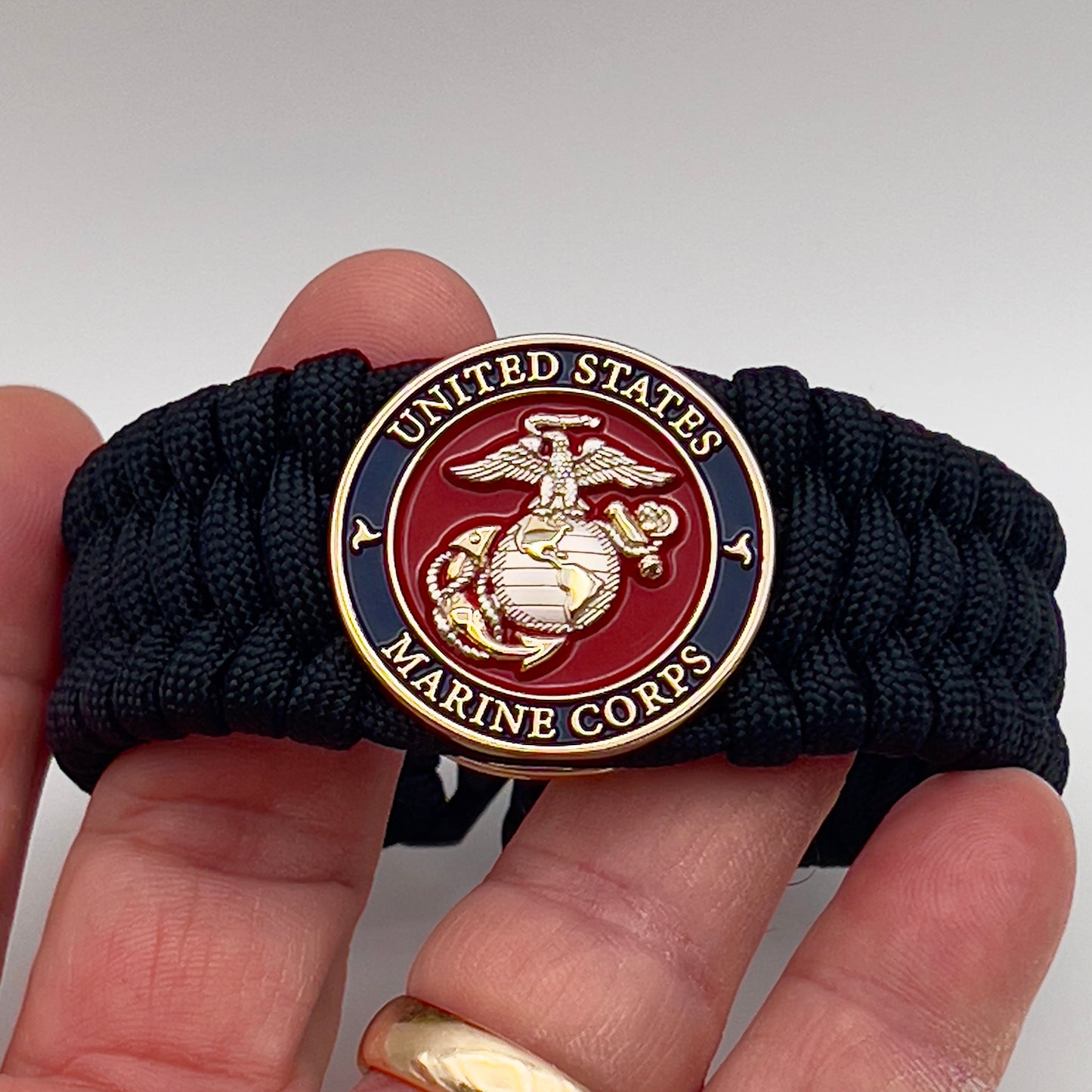 Thick and comfortable braided United States Marine Corps bracelet featuring a 24K gold and silver plated USMC officer Eagle Globe and Anchor medallion, a black Cobra style tactical buckle and woven with black 550 paracord.