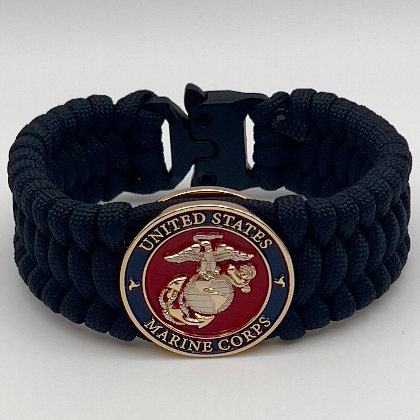 Thick and comfortable braided United States Marine Corps bracelet featuring a 24K gold and silver plated USMC officer Eagle Globe and Anchor medallion, a black Cobra style tactical buckle and woven with black 550 paracord.