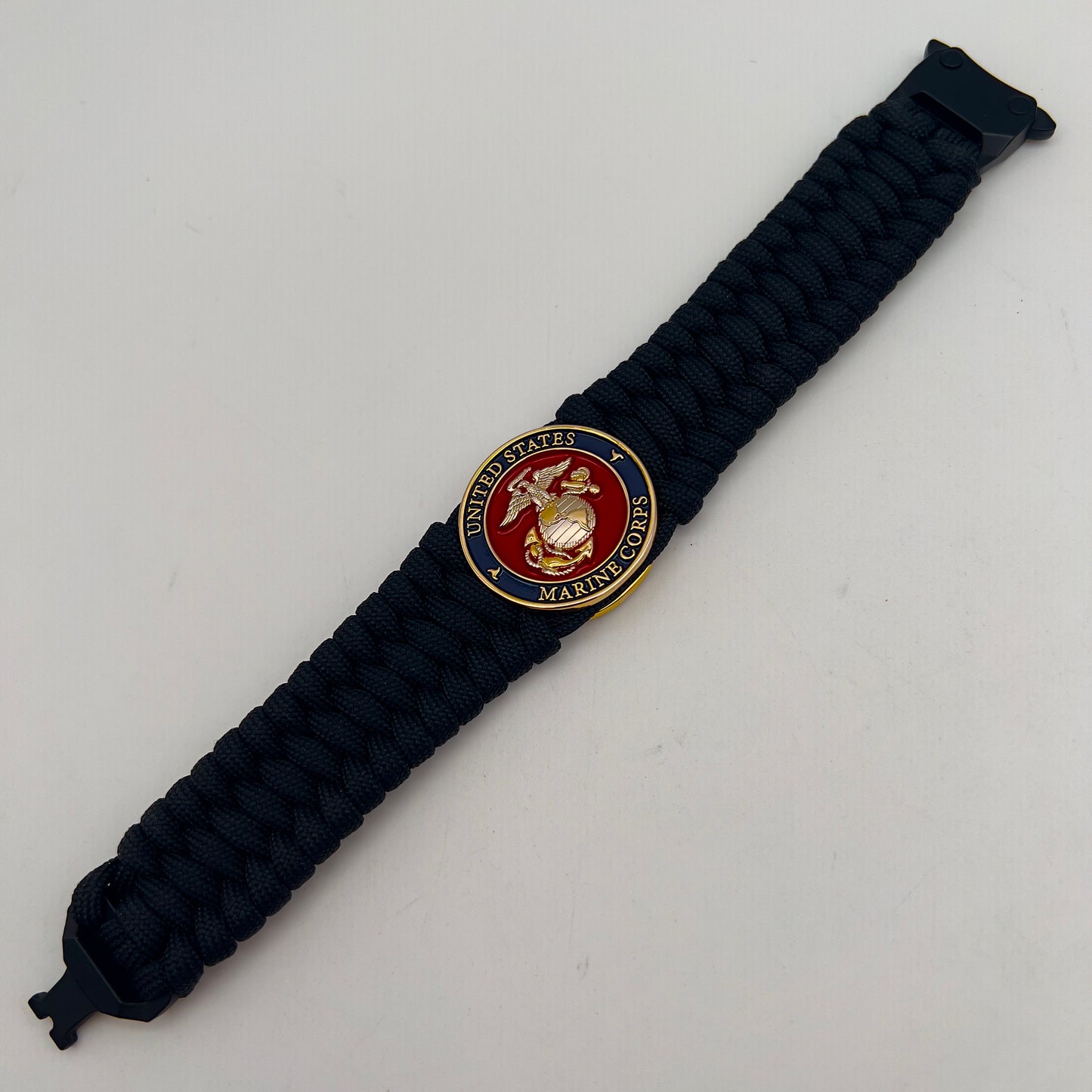 Thick and comfortable braided United States Marine Corps bracelet featuring a 24K gold and silver plated USMC officer Eagle Globe and Anchor medallion, a black Cobra style tactical buckle and woven with black 550 paracord.