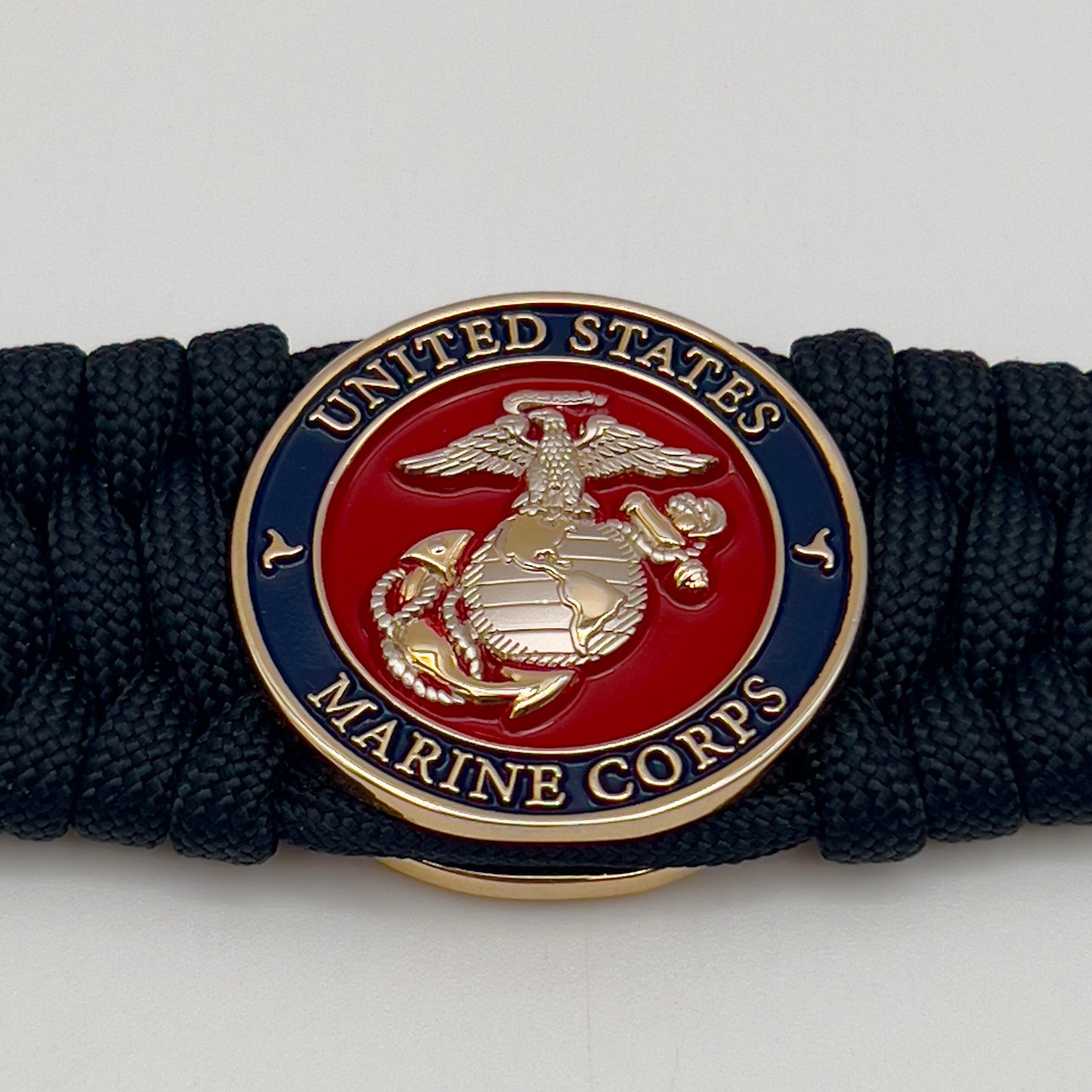 Thick and comfortable braided United States Marine Corps bracelet featuring a 24K gold and silver plated USMC officer Eagle Globe and Anchor medallion, a black Cobra style tactical buckle and woven with black 550 paracord.