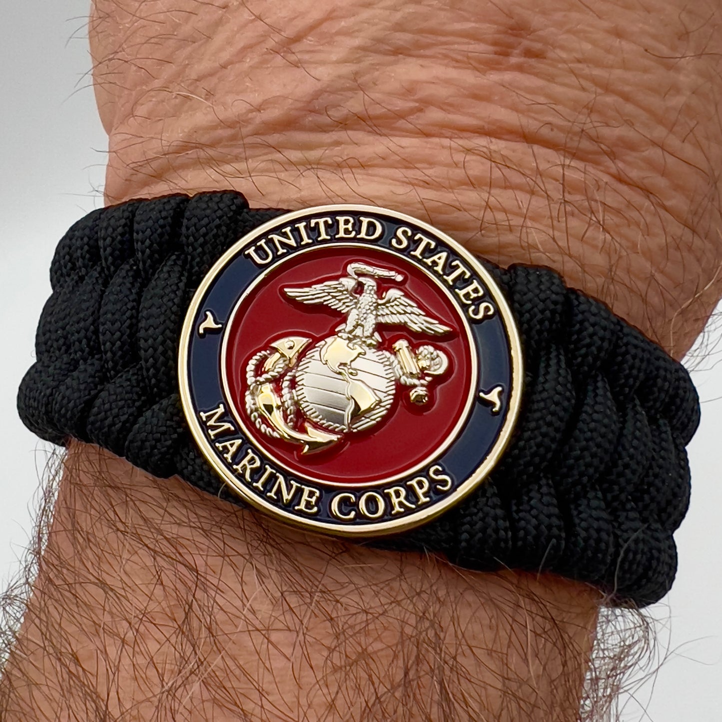 Thick and comfortable braided United States Marine Corps bracelet featuring a 24K gold and silver plated USMC officer Eagle Globe and Anchor medallion, a black Cobra style tactical buckle and woven with black 550 paracord.