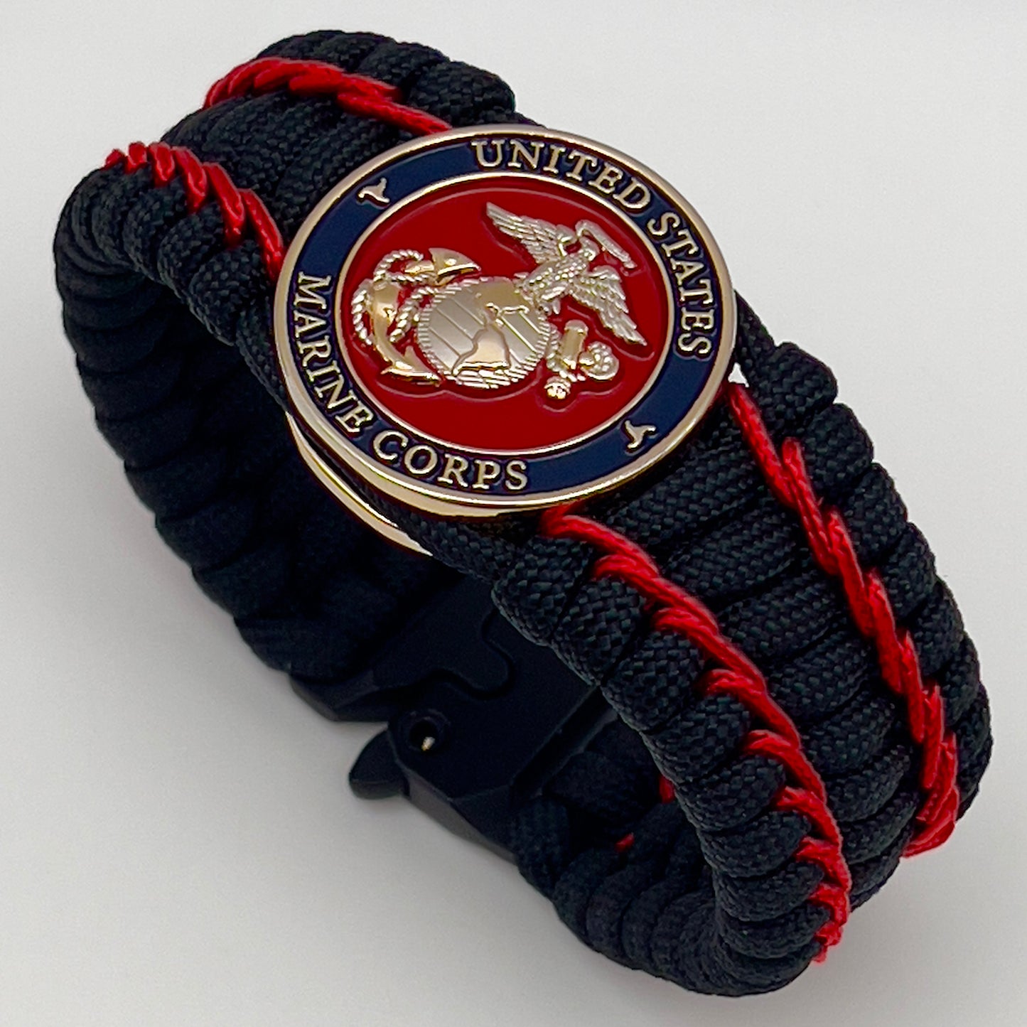 Thick and comfortable braided United States Marine Corps bracelet featuring a 24K gold and silver plated USMC officer Eagle Globe and Anchor medallion, a black Cobra style tactical buckle and woven with black 550 paracord and Imperial Red micro cord.