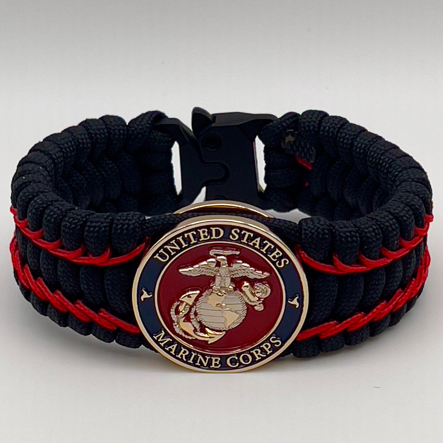 Thick and comfortable braided United States Marine Corps bracelet featuring a 24K gold and silver plated USMC officer Eagle Globe and Anchor medallion, a black Cobra style tactical buckle and woven with black 550 paracord and Imperial Red micro cord.