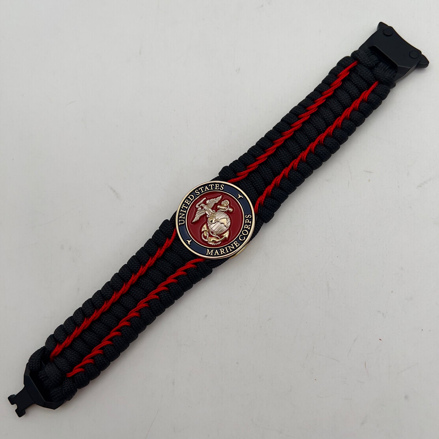 Thick and comfortable braided United States Marine Corps bracelet featuring a 24K gold and silver plated USMC officer Eagle Globe and Anchor medallion, a black Cobra style tactical buckle and woven with black 550 paracord and Imperial Red micro cord.