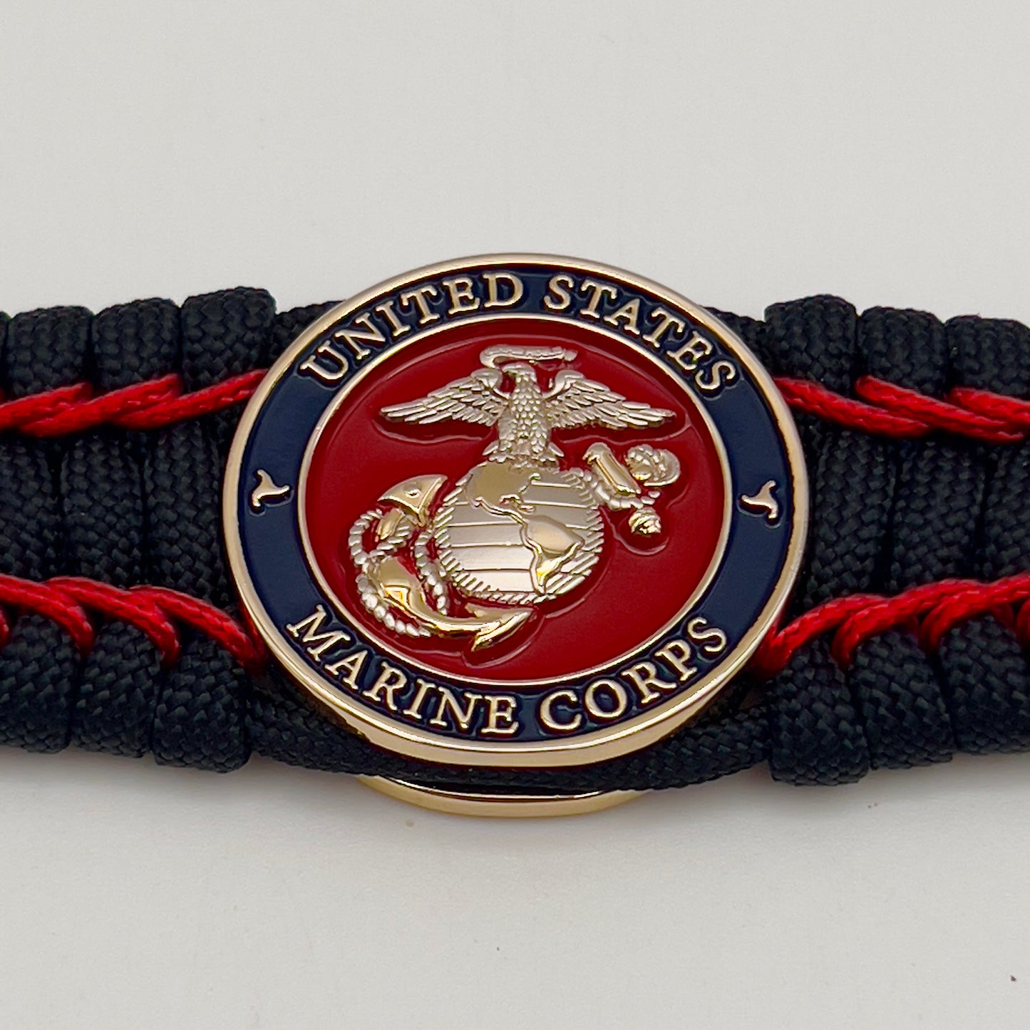 Thick and comfortable braided United States Marine Corps bracelet featuring a 24K gold and silver plated USMC officer Eagle Globe and Anchor medallion, a black Cobra style tactical buckle and woven with black 550 paracord and Imperial Red micro cord.