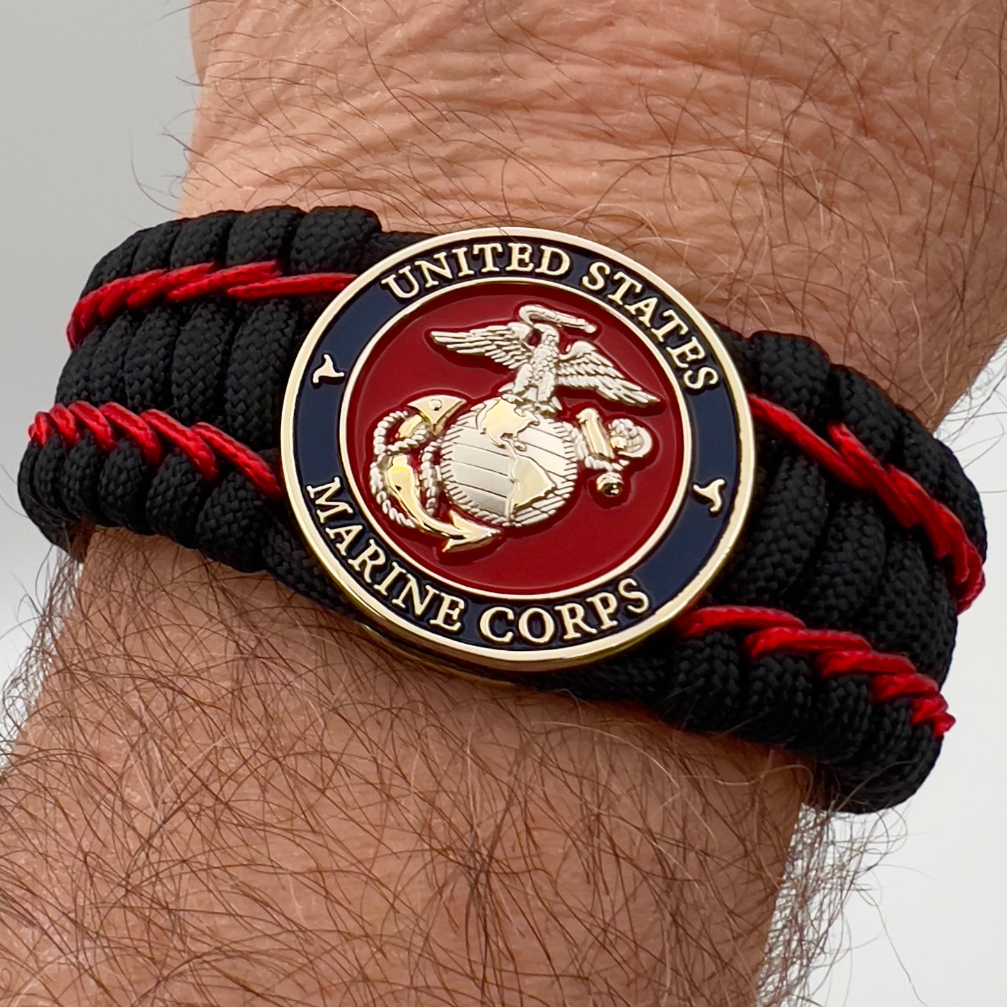 Thick and comfortable braided United States Marine Corps bracelet featuring a 24K gold and silver plated USMC officer Eagle Globe and Anchor medallion, a black Cobra style tactical buckle and woven with black 550 paracord and Imperial Red micro cord.