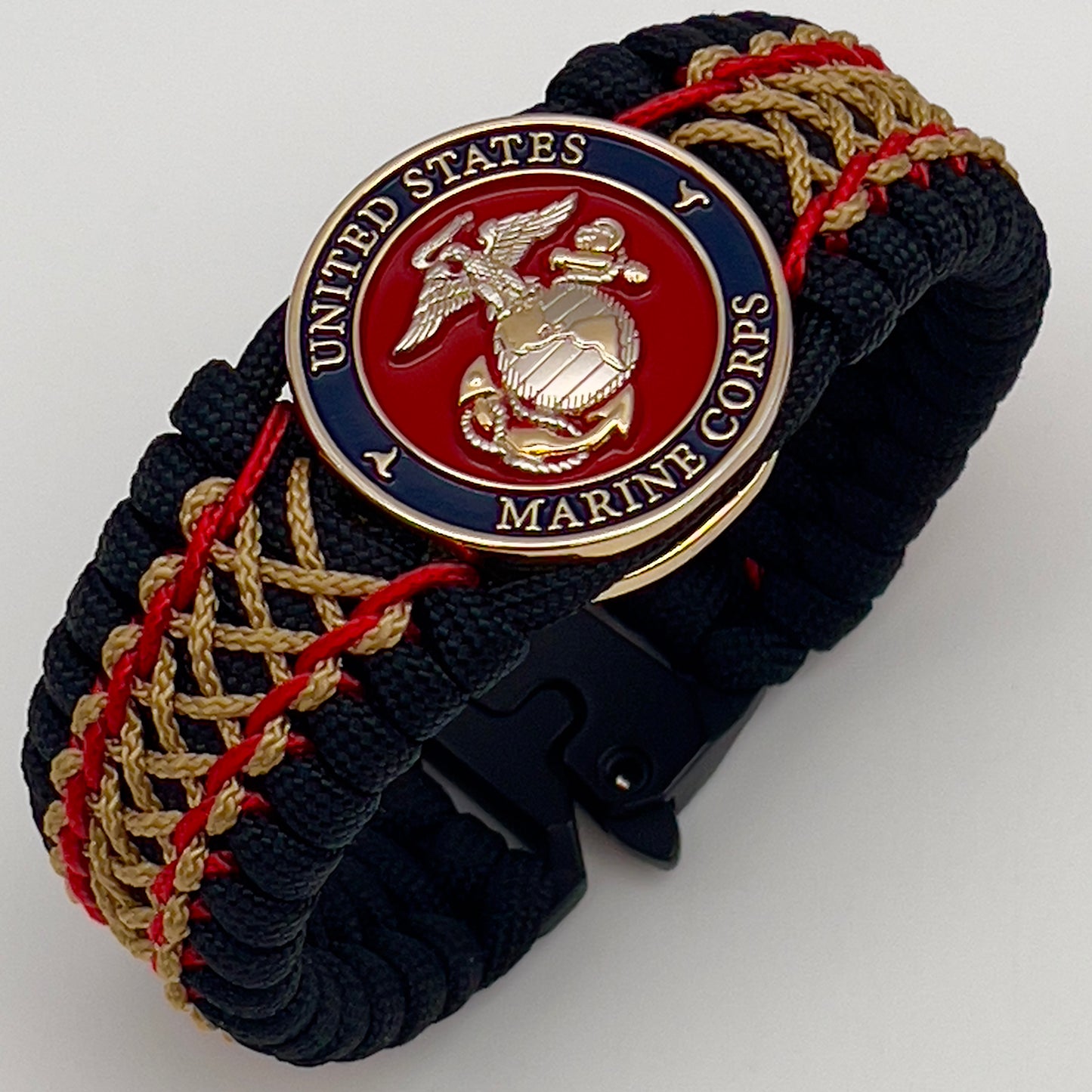 Thick and comfortable braided United States Marine Corps bracelet featuring a 24K gold and silver plated USMC officer Eagle Globe and Anchor medallion, a black Cobra style tactical buckle and woven with black 550 paracord and Imperial Red and gold micro cord.