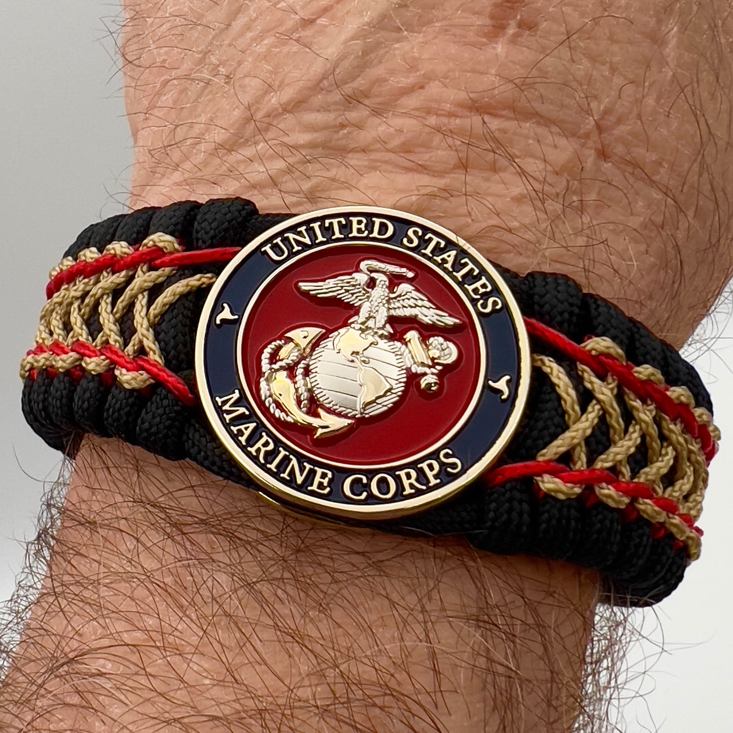 Thick and comfortable braided United States Marine Corps bracelet featuring a 24K gold and silver plated USMC officer Eagle Globe and Anchor medallion, a black Cobra style tactical buckle and woven with black 550 paracord and Imperial Red and gold micro cord.
