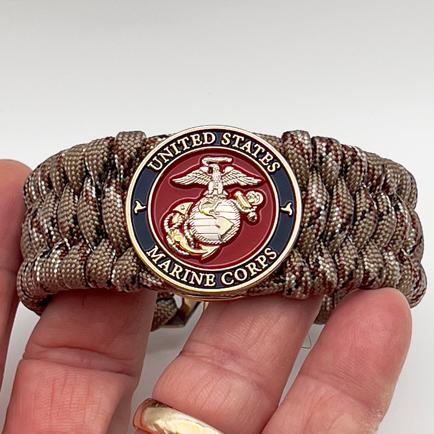 Thick and comfortable braided United States Marine Corps bracelet featuring a 24K gold and silver plated USMC officer Eagle Globe and Anchor medallion, a gold Cobra style tactical buckle and woven with Desert Camo 550 paracord.