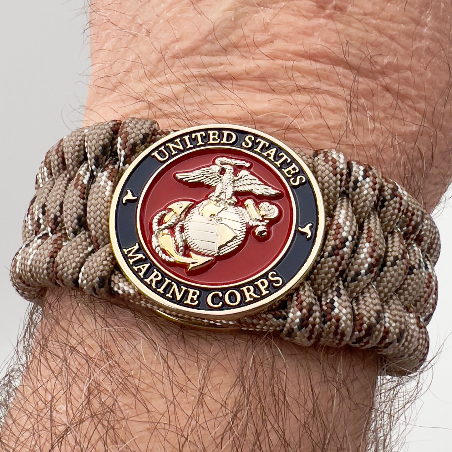 Thick and comfortable braided United States Marine Corps bracelet featuring a 24K gold and silver plated USMC officer Eagle Globe and Anchor medallion, a gold Cobra style tactical buckle and woven with Desert Camo 550 paracord.