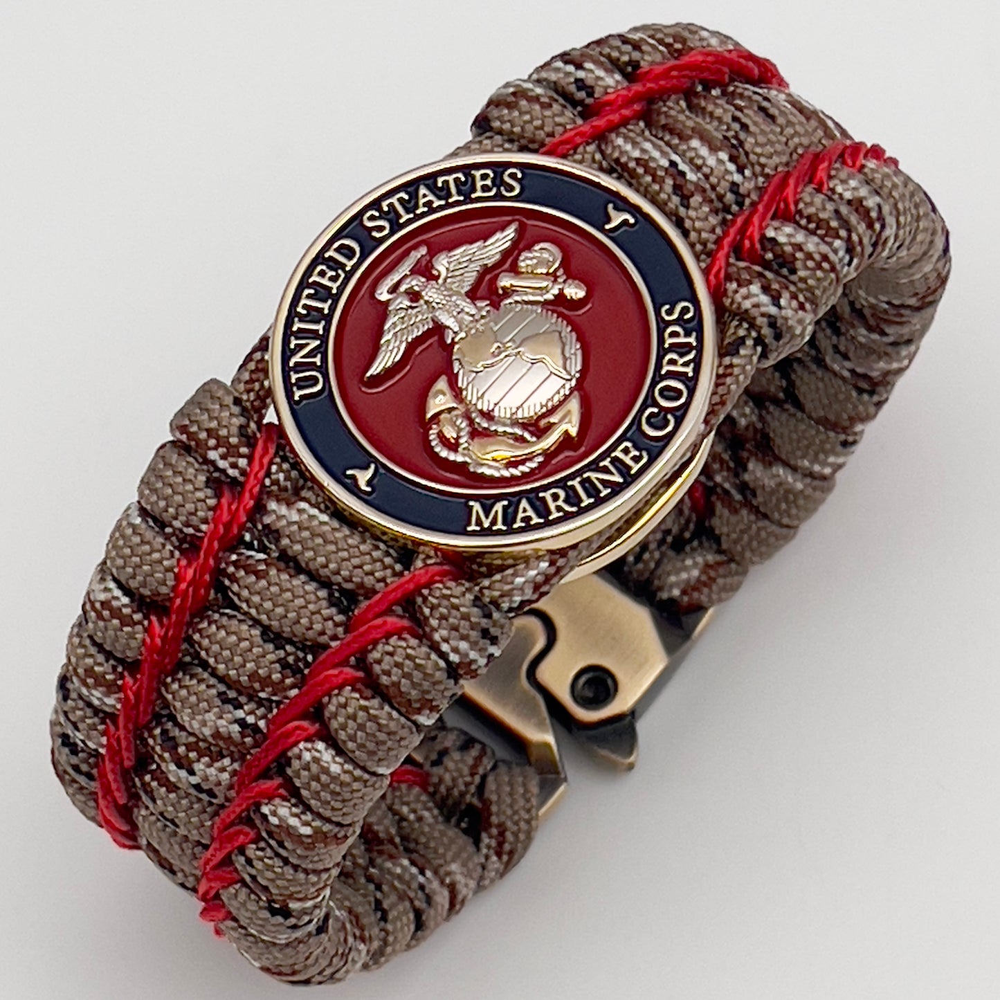 Thick and comfortable braided United States Marine Corps bracelet featuring a 24K gold and silver plated USMC officer Eagle Globe and Anchor medallion, a gold Cobra style tactical buckle and woven with Desert Camo 550 paracord and Imperial Red micro cord.