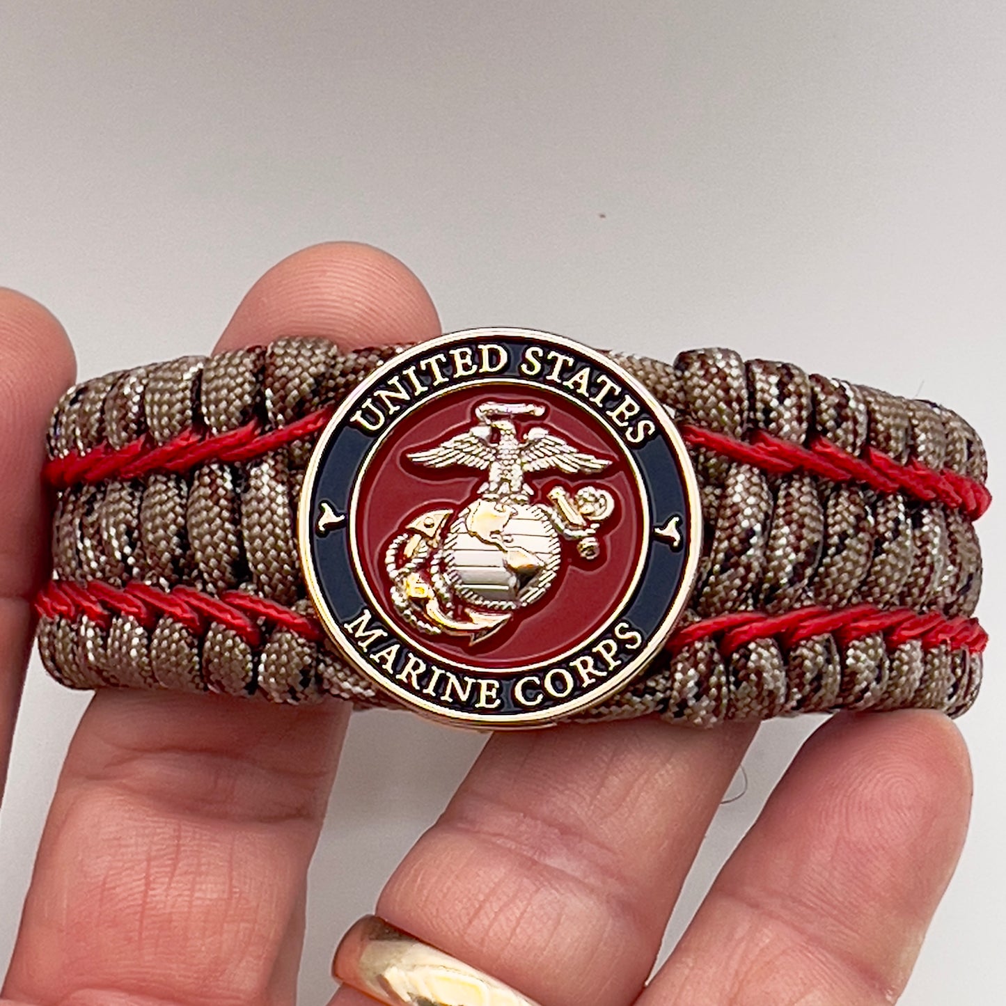 Thick and comfortable braided United States Marine Corps bracelet featuring a 24K gold and silver plated USMC officer Eagle Globe and Anchor medallion, a gold Cobra style tactical buckle and woven with Desert Camo 550 paracord and Imperial Red micro cord.
