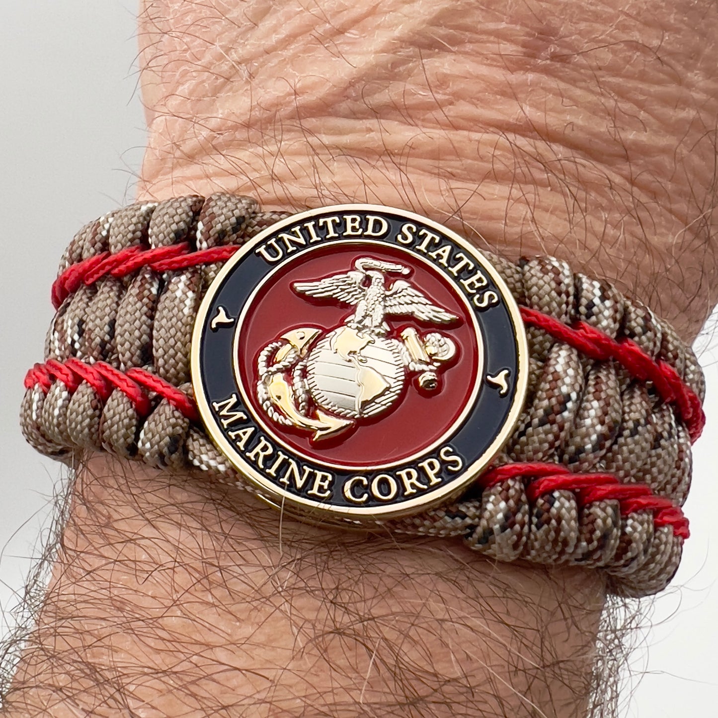 Thick and comfortable braided United States Marine Corps bracelet featuring a 24K gold and silver plated USMC officer Eagle Globe and Anchor medallion, a gold Cobra style tactical buckle and woven with Desert Camo 550 paracord and Imperial Red micro cord.