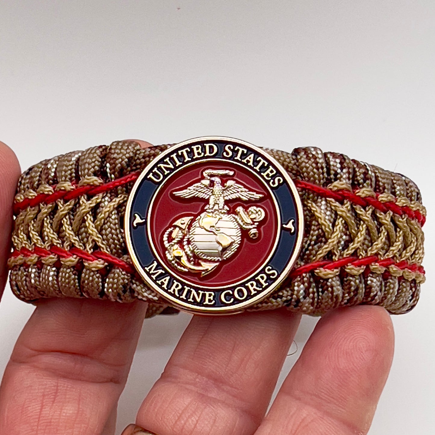 Thick and comfortable braided United States Marine Corps bracelet featuring a 24K gold and silver plated USMC officer Eagle Globe and Anchor medallion, a gold Cobra style tactical buckle and woven with Desert Camo 550 paracord and Imperial Red and Gold micro cord.