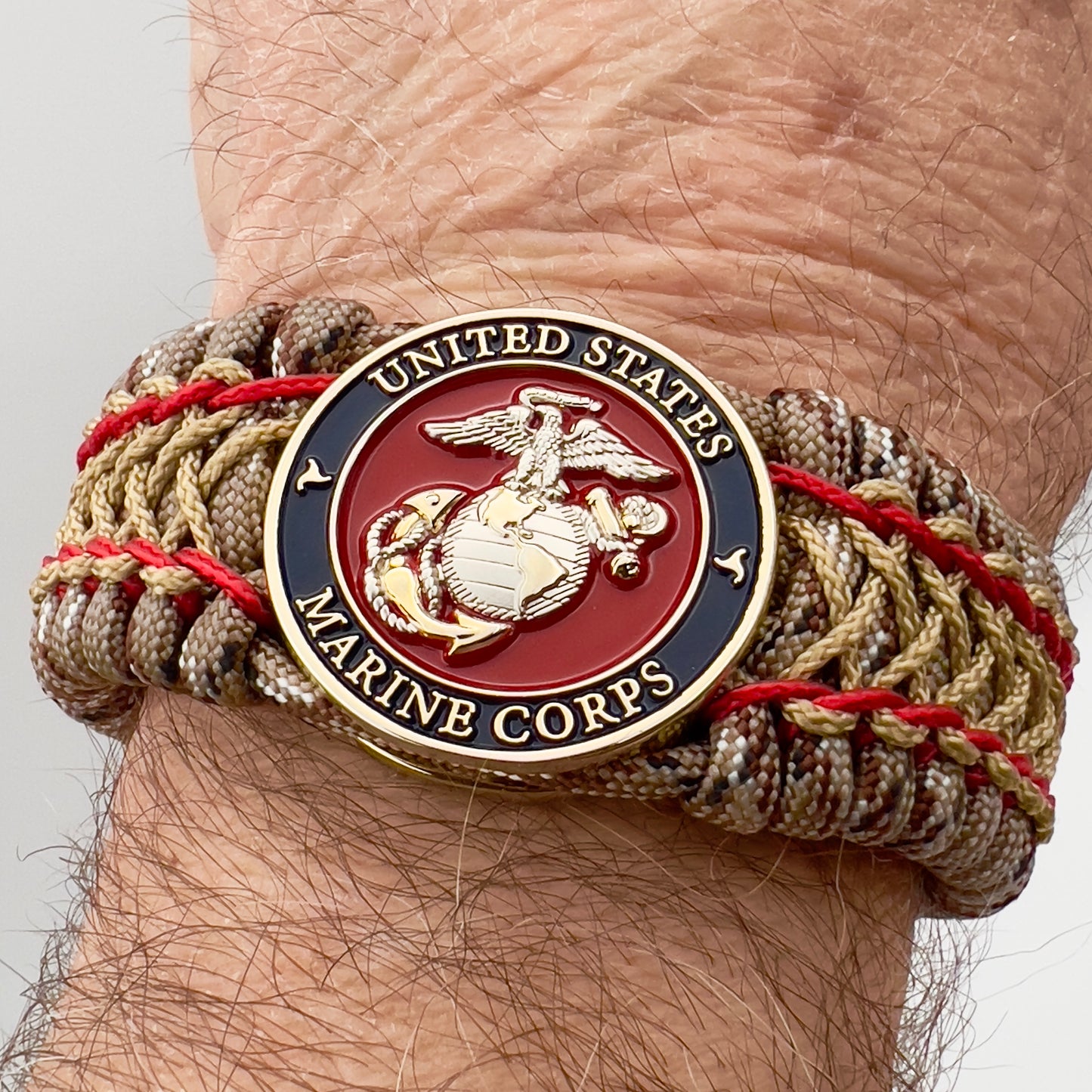 Thick and comfortable braided United States Marine Corps bracelet featuring a 24K gold and silver plated USMC officer Eagle Globe and Anchor medallion, a gold Cobra style tactical buckle and woven with Desert Camo 550 paracord and Imperial Red and Gold micro cord.
