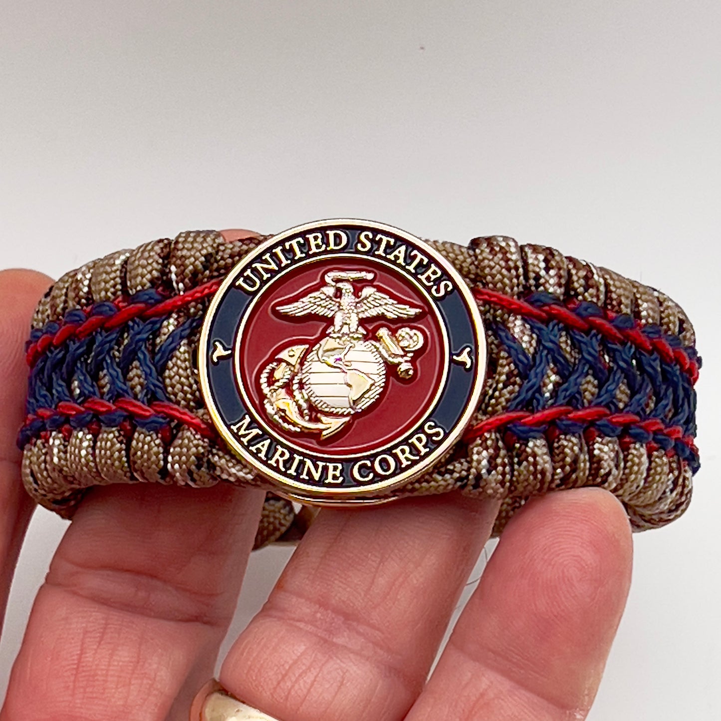 Thick and comfortable braided United States Marine Corps bracelet featuring a 24K gold and silver plated USMC officer Eagle Globe and Anchor medallion, a gold Cobra style tactical buckle and woven with Desert Camo 550 paracord and Imperial Red and Navy Blue micro cord.